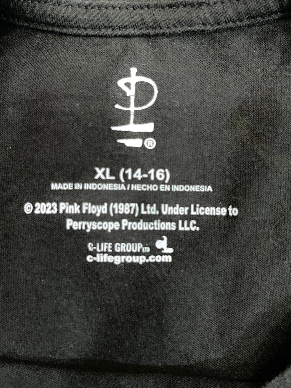 Close-up of the inside neck label of a black garment, showing white printed text including 'XL (14-16)', 'MADE IN INDONESIA', copyright details, and the Perryscope logo.