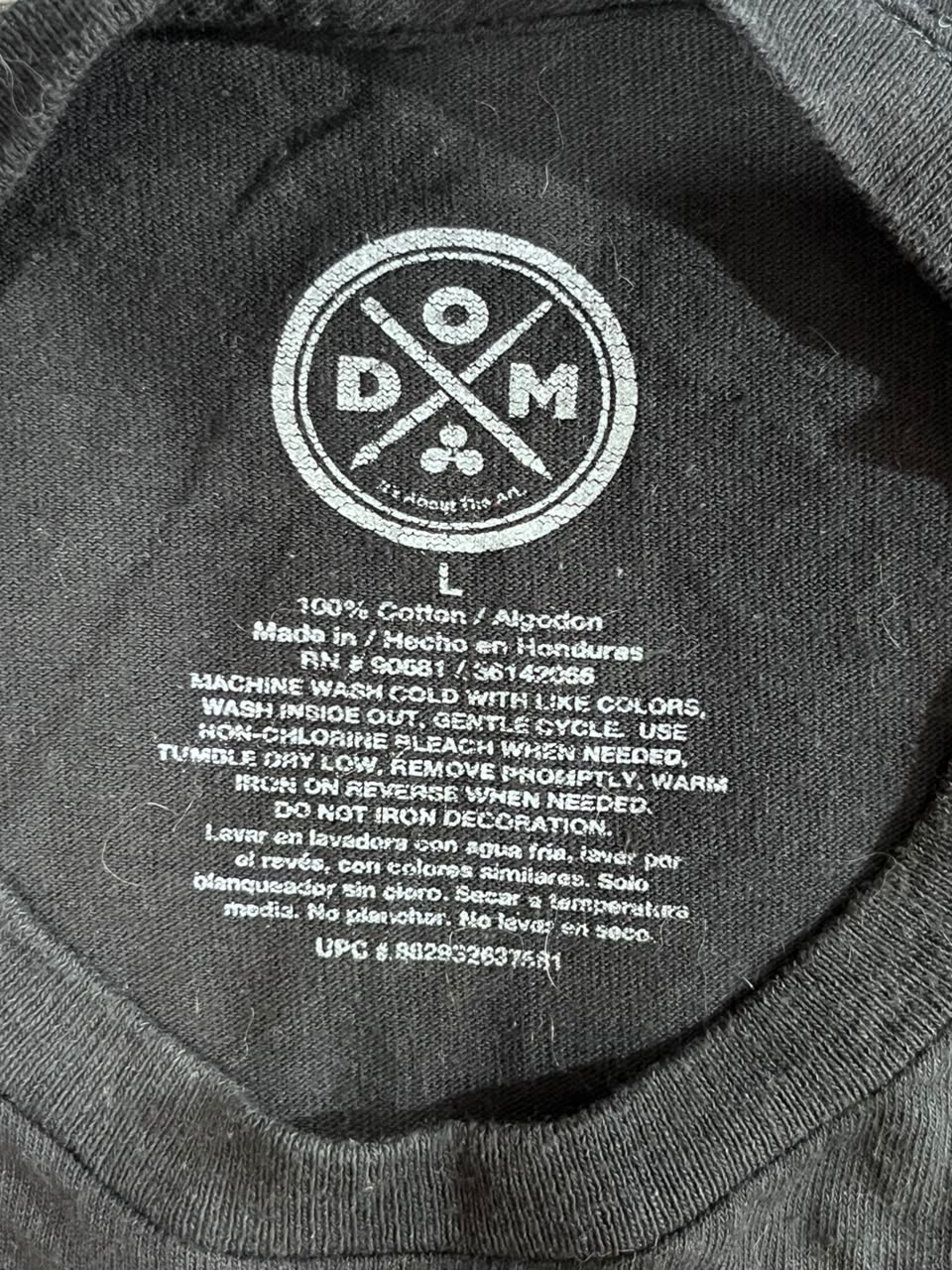 Close-up of the inside collar of a dark gray t-shirt showing the printed white care label with the brand 'Domestic Made' and care instructions.