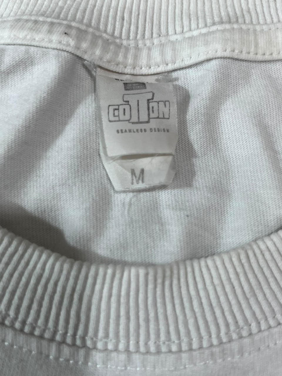 Close-up of a white ribbed knit garment neck with a sewn-in fabric tag reading COTTON and M.