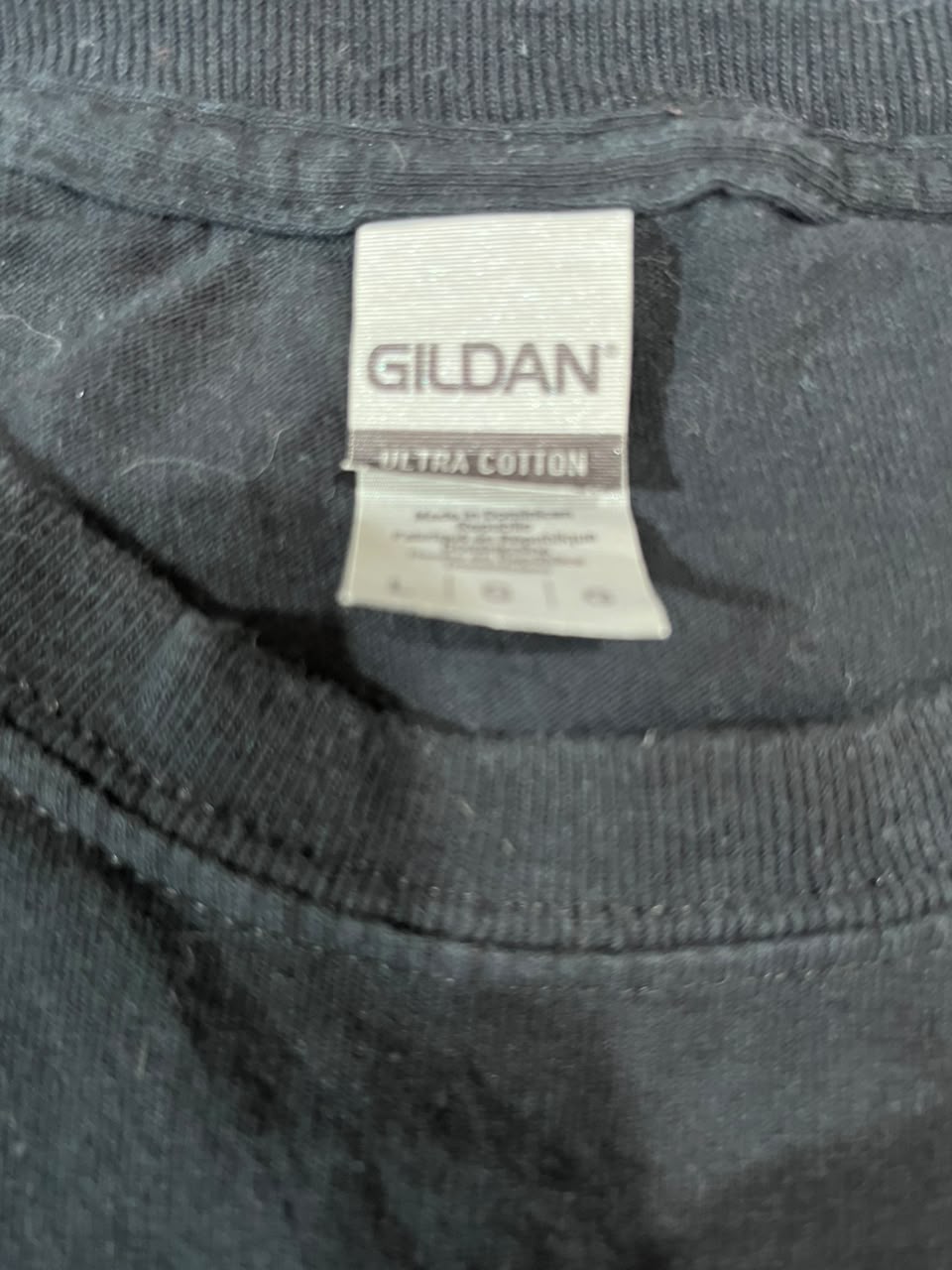 Close-up of a dark gray or black Gildan ultra cotton t-shirt neck label, showing the brand name Gildan and fabric type details.