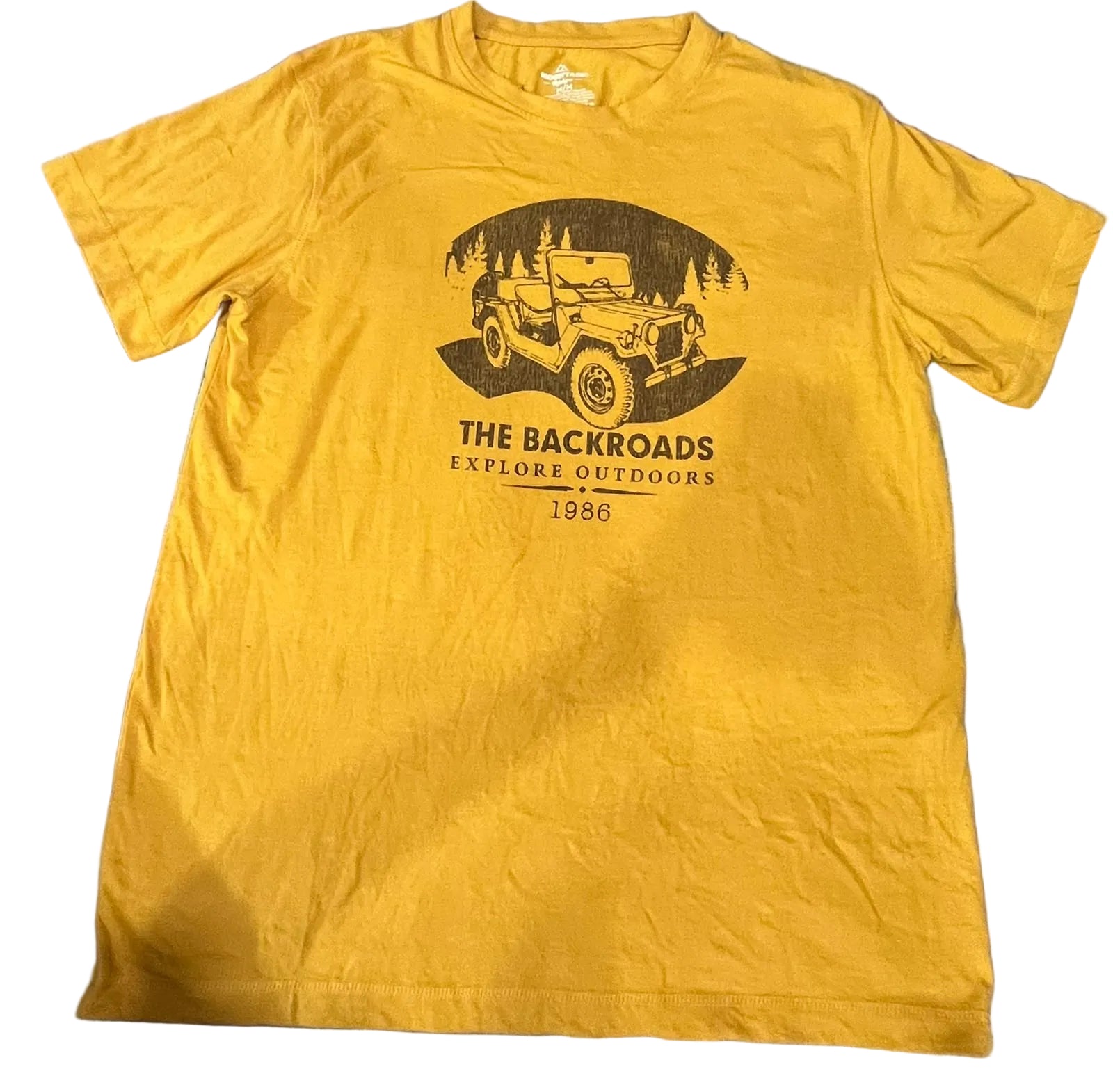 A yellow short-sleeve graphic t-shirt  The shirt features a black graphic of a vintage jeep in a forest with the text 'THE BACKROADS EXPLORE OUTDOORS 1986'.