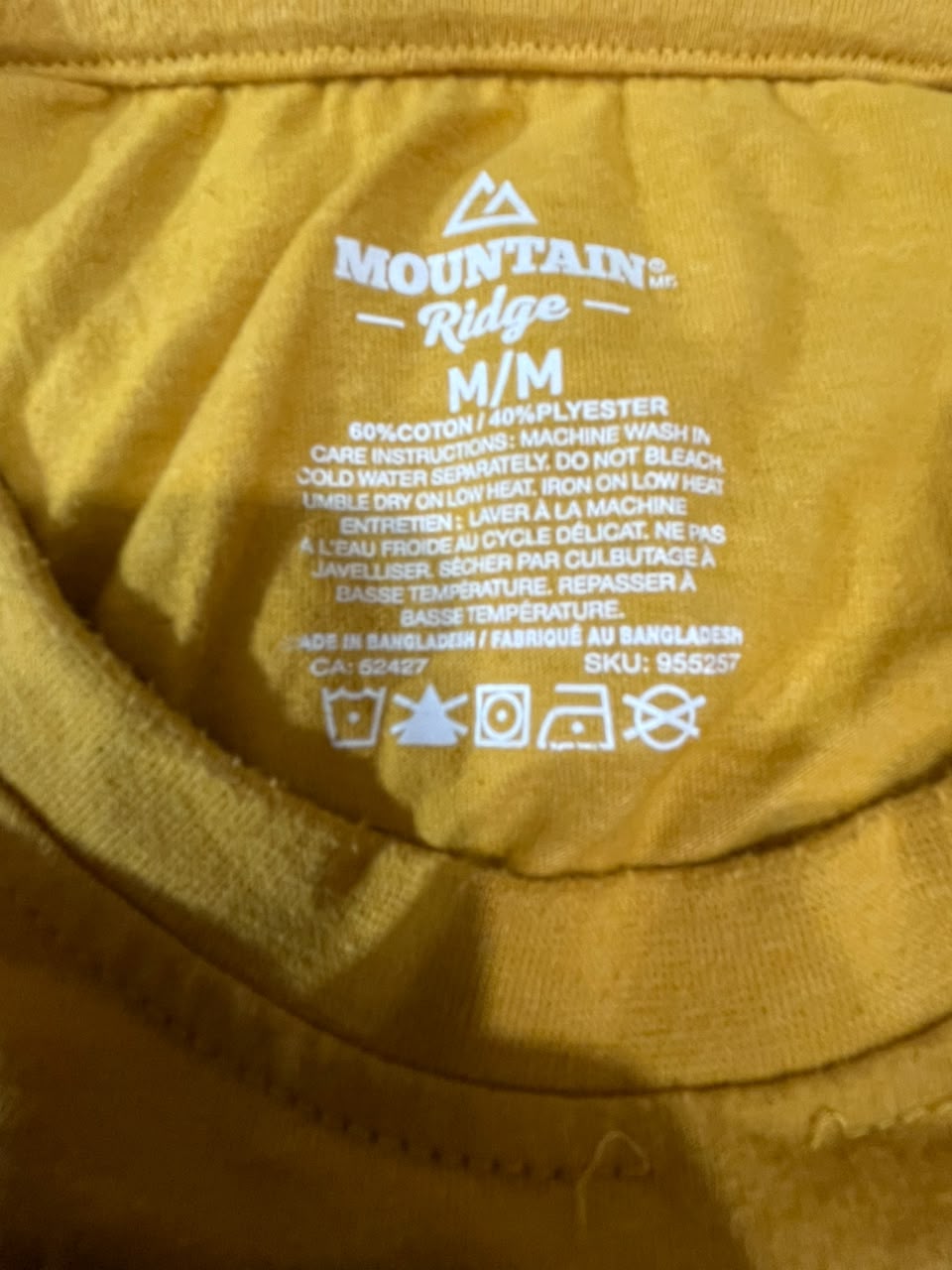 Close-up of the inside neck label of a yellow Mountain Ridge t-shirt, showing the size M/M and care instructions printed in white.