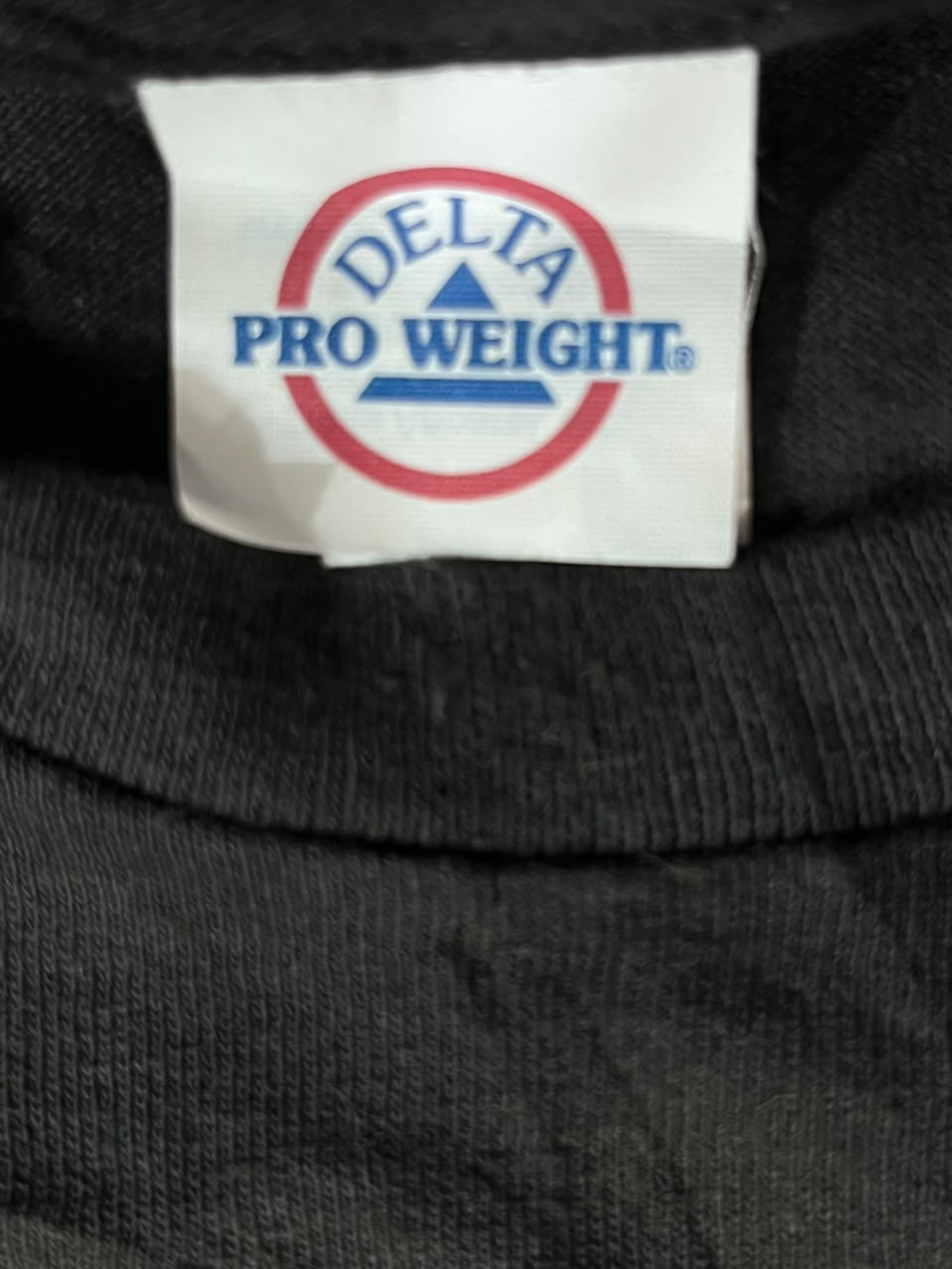 Close-up of a black ribbed knit garment collar with a white Delta Pro Weight brand tag sewn inside.