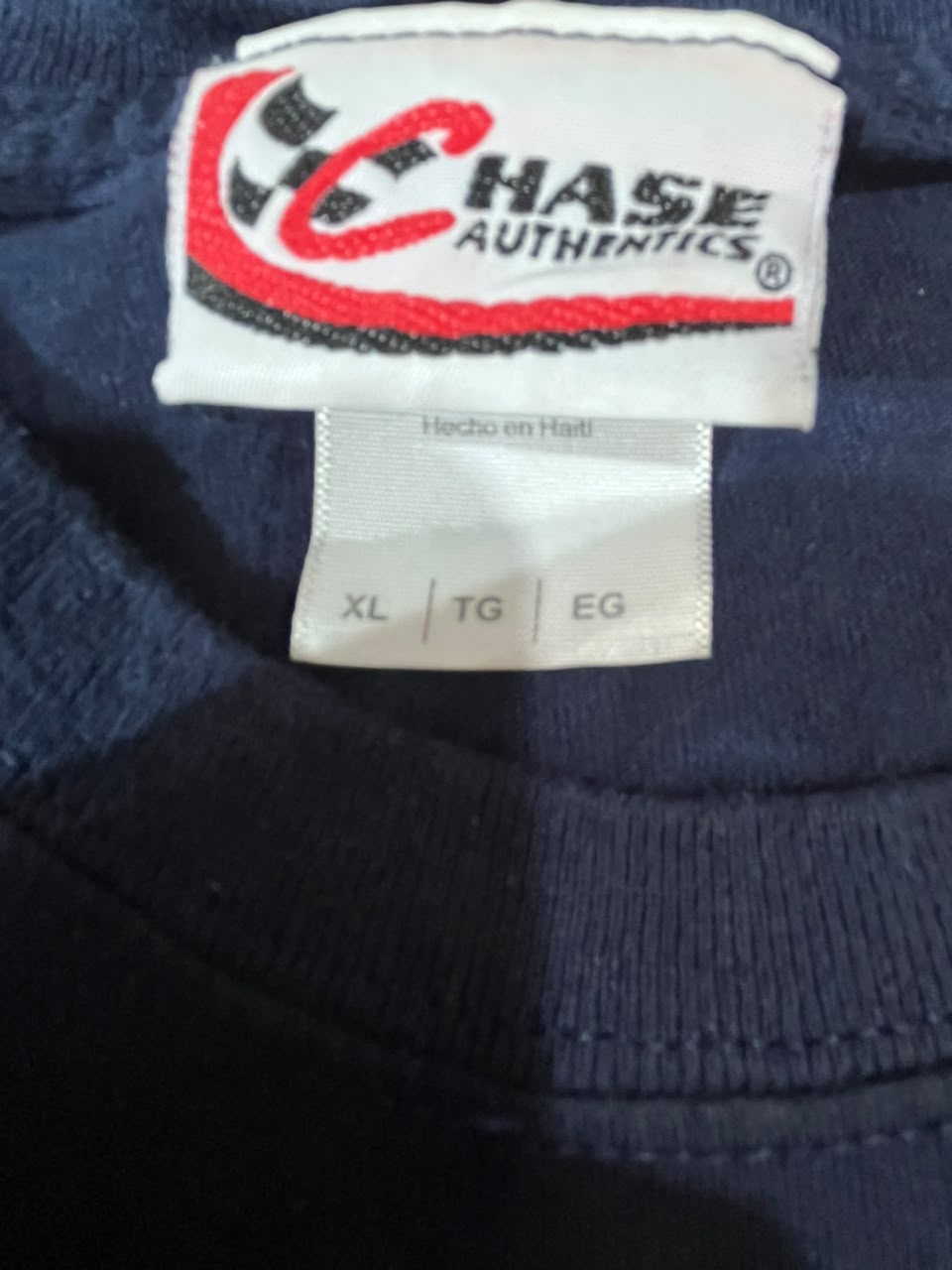 Close-up of a navy blue garment neck label showing the Chase Authentics logo and size information including XL, TG, and EG.