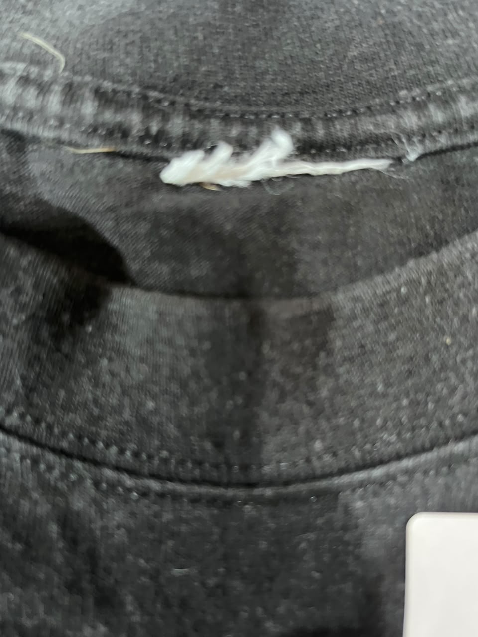 Close-up of a dark gray or black knit fabric with visible stitching and a small white lint or fiber caught near the center.
