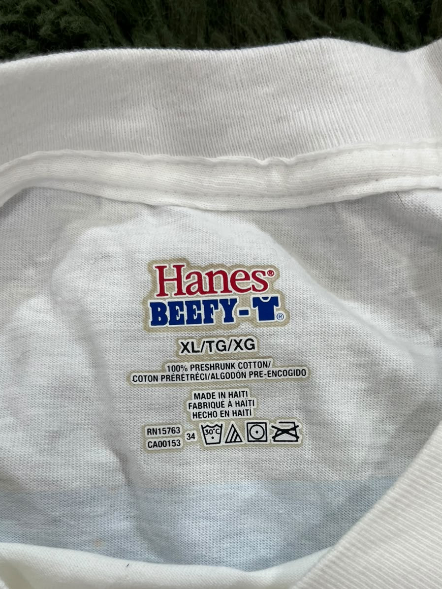 Close-up of the inside collar of a white Hanes Beefy T-shirt, showing the brand label and care instructions, with a finger pointing at the bottom.