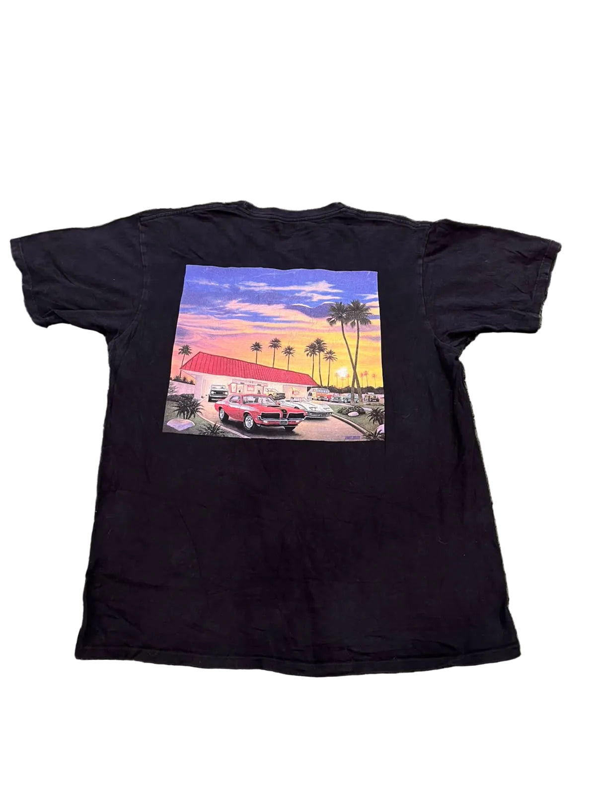 A black short-sleeve t-shirt  featuring a large square graphic print on the back with a retro red car, palm trees, and a colorful sunset sky.