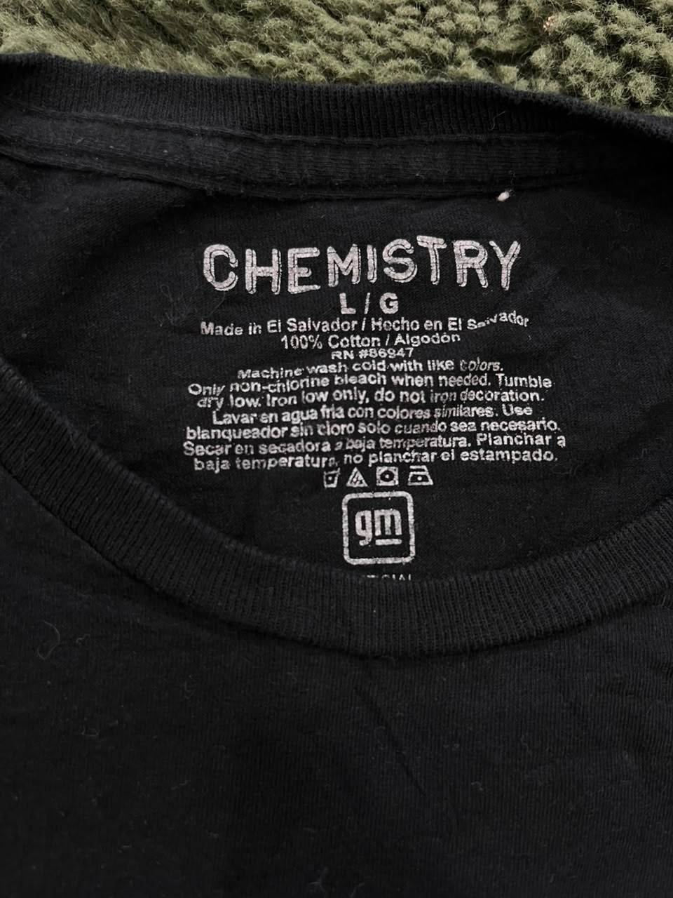 Close-up of the inside collar of a black t-shirt showing the printed neck label with 'CHEMISTRY L.G' and care instructions.
