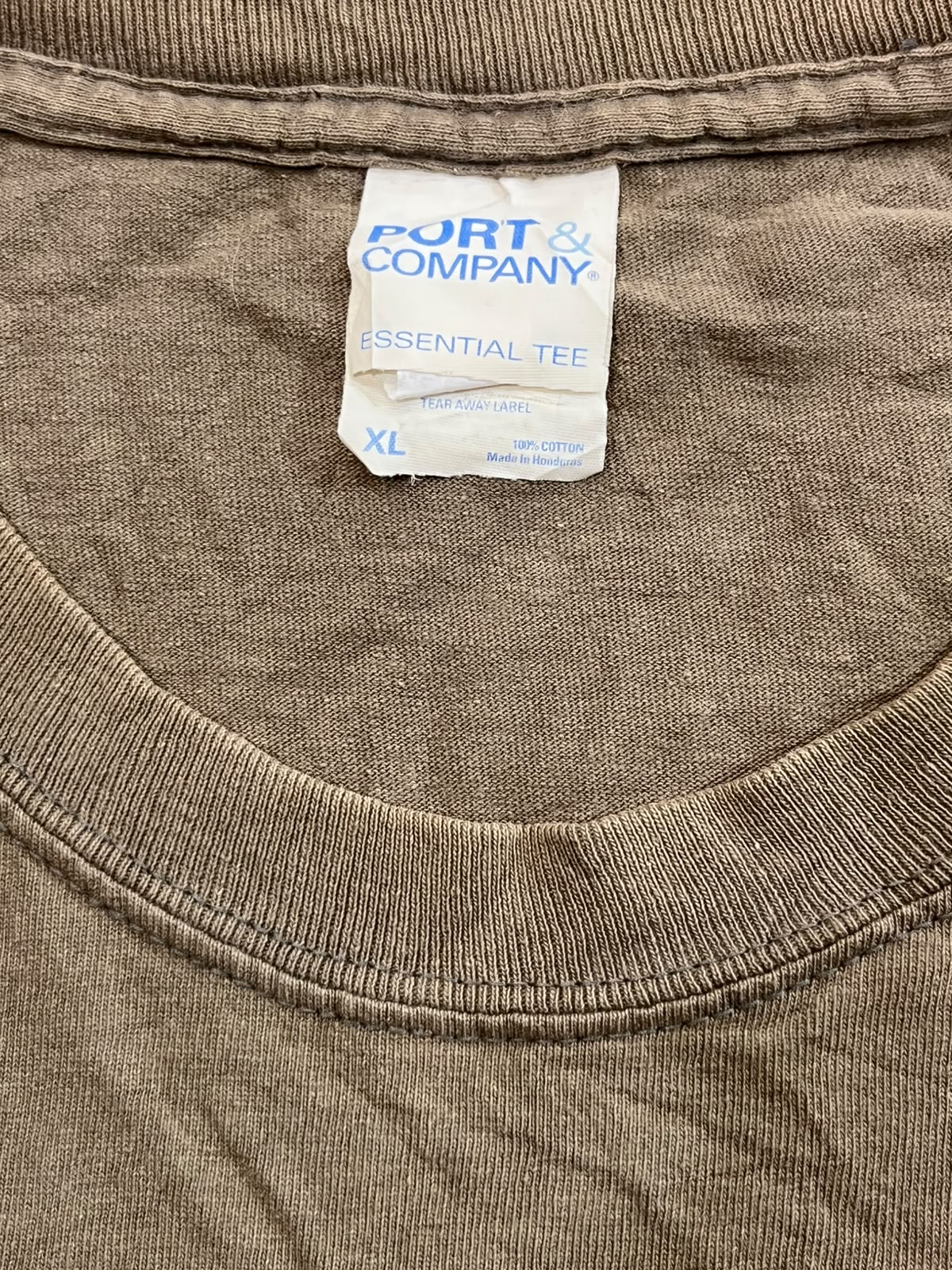 Close-up of the inside collar of a brown cotton t-shirt showing the Port & Company Essential Tee tag.