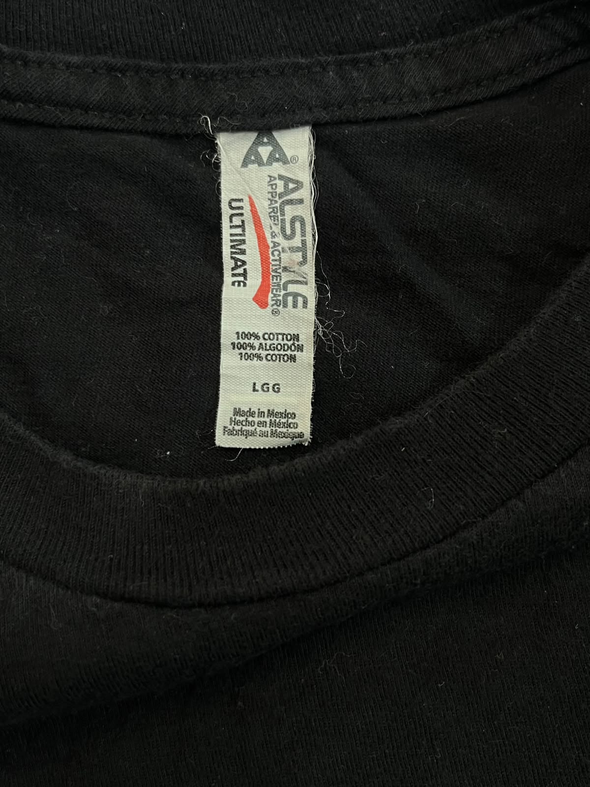 Close-up of the inside neck label of a black cotton t-shirt. The brand 'ASTMILE' is clearly visible on the white tag.