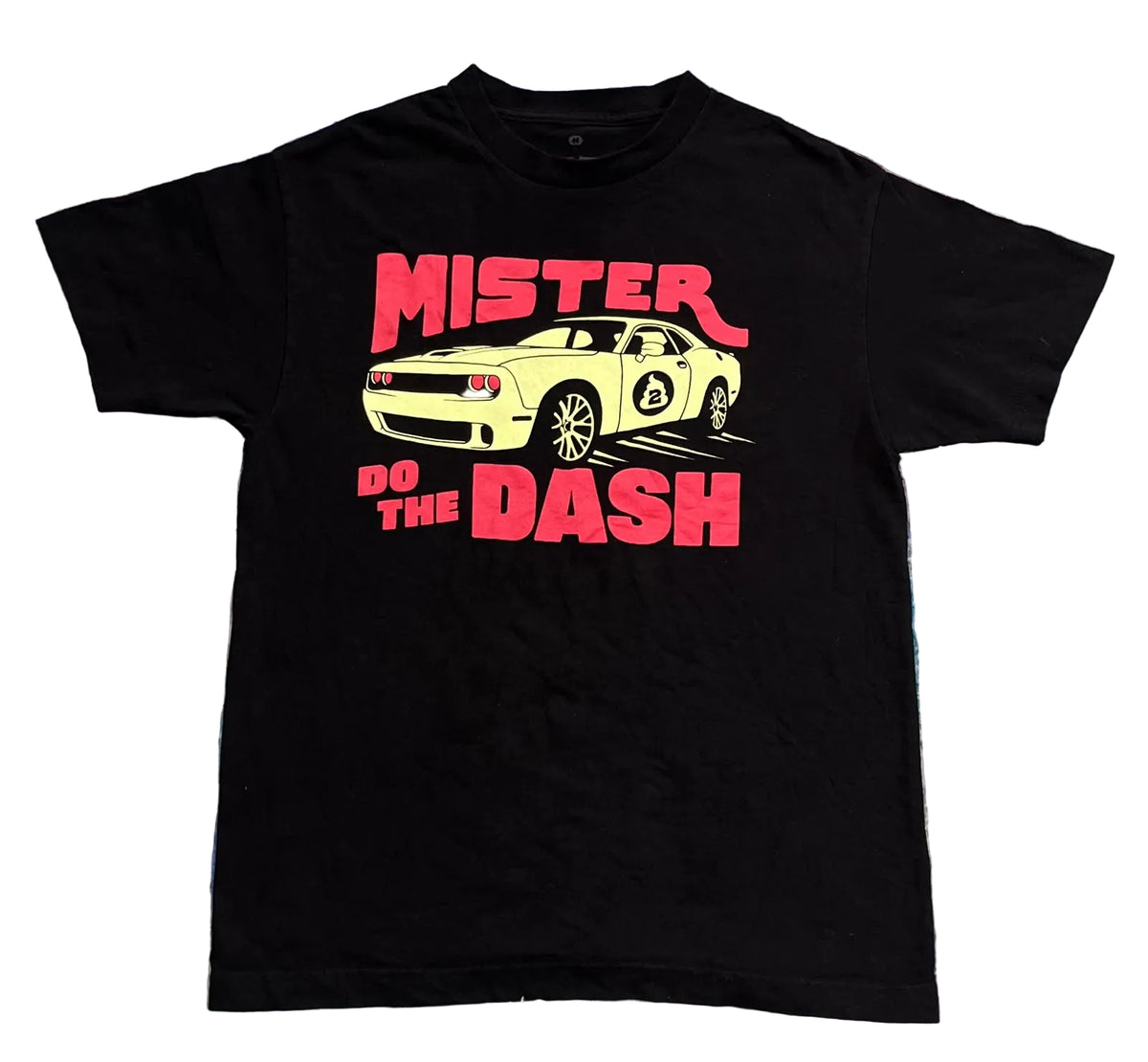 A black short-sleeve graphic t-shirt. The graphic features a yellow car with the text 'MISTER DO THE DASH' in bright pink.