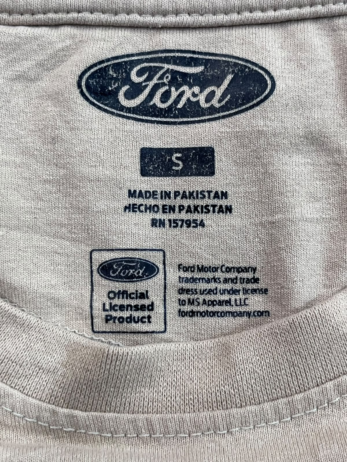 Close-up of the inside neck label of a light beige Ford t-shirt, showing the size 5 label, 'Made in Pakistan' text, and an 'Official Licensed Product' badge.
