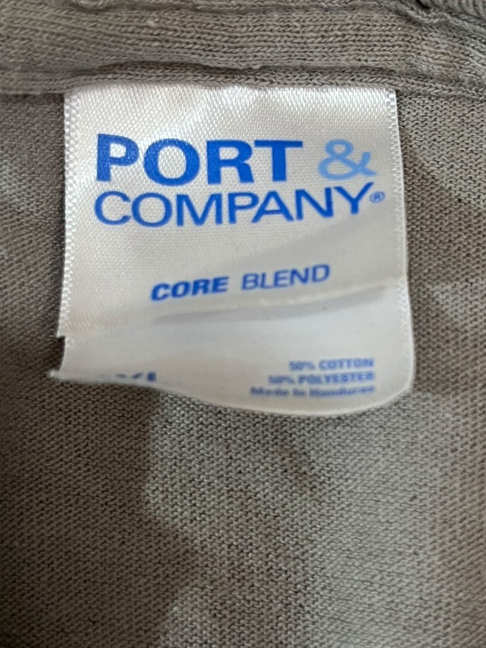 Close-up of a garment's interior neck label reading PORT & COMPANY CORE BLEND, sewn onto a textured gray fabric.