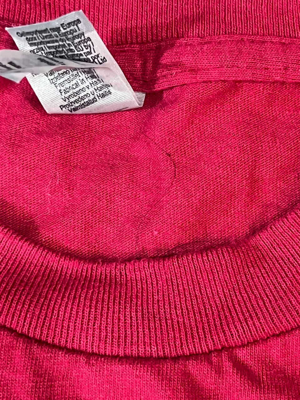 Close-up of a bright pink knit garment showing the inner neck area, ribbed collar, and a white sewn-in care label.