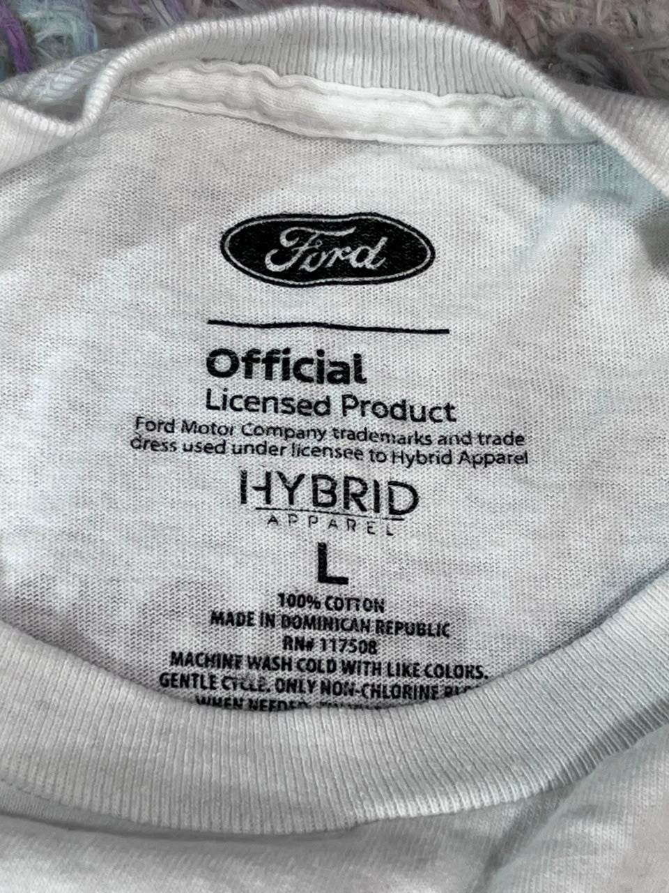 Close-up of the inside neck label of a white Ford Hybrid T-shirt, showing the Ford logo and product details.