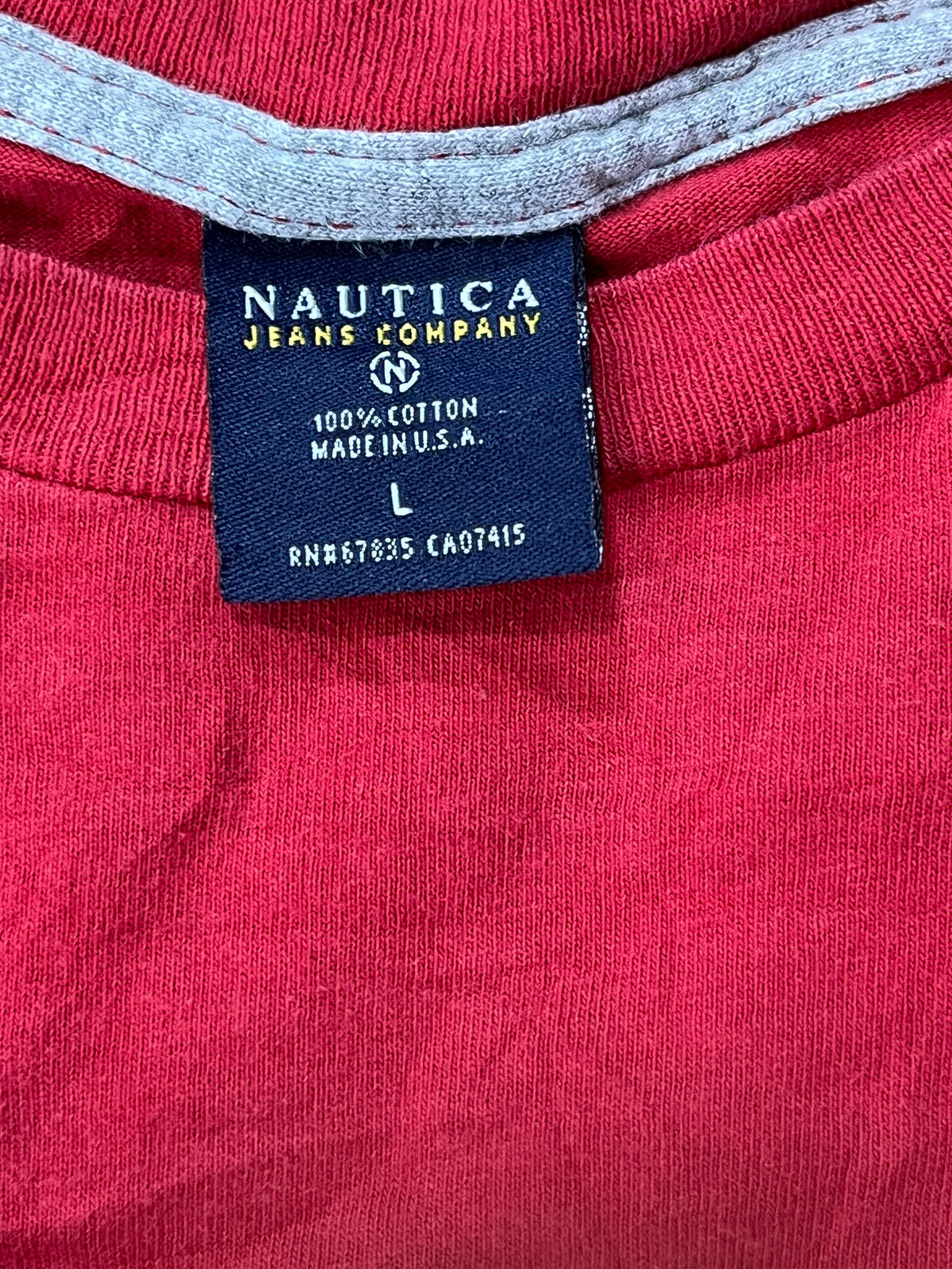 Close-up of a red garment with a visible navy Nautica brand label sewn inside the collar, next to a light gray ribbed trim.