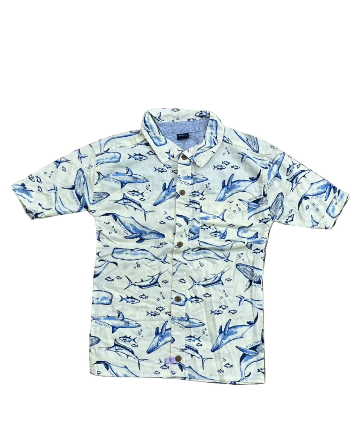 A children's long-sleeve button-up shirt with a blue whale and fish print on a cream-colored fabric,A person's feet are visible at the top edge of the frame.
