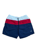 Colorblock swim trunks with a white top section, a red middle band, and a navy blue bottom section, A small white sailboat logo is visible on the lower left leg.