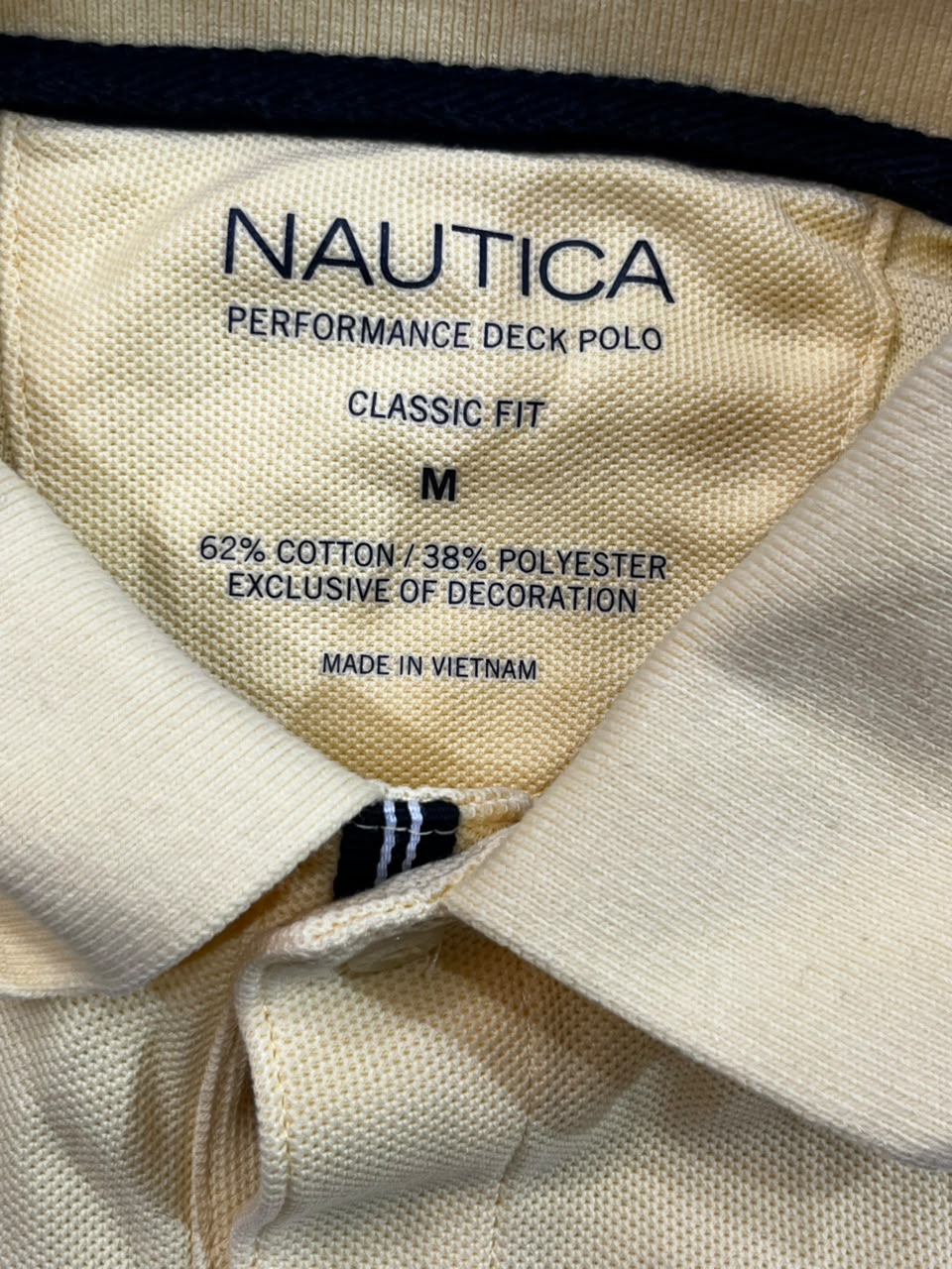 Close-up of the inside collar of a Nautica Performance Deck Polo shirt, showing the cream-colored fabric and navy blue printed text with size information.