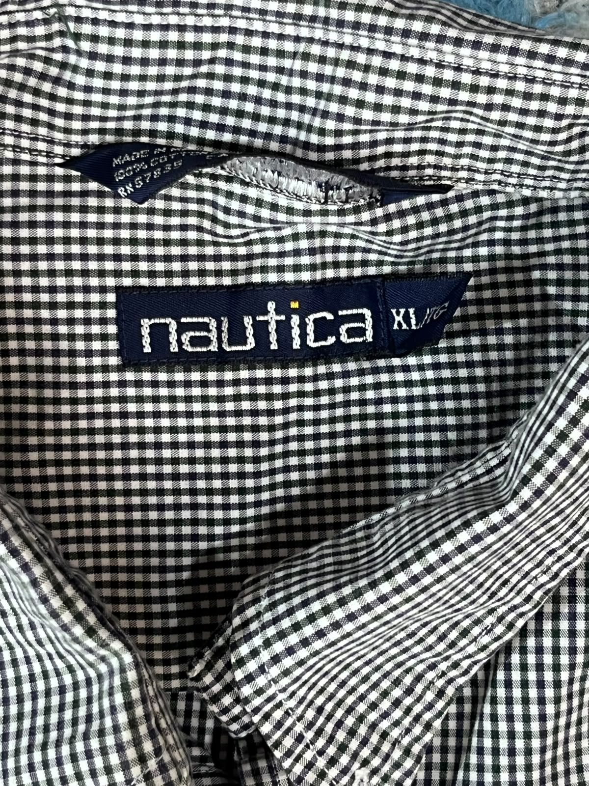 Close-up of a Nautica gingham shirt collar showing the navy blue brand label with white text and size XL.