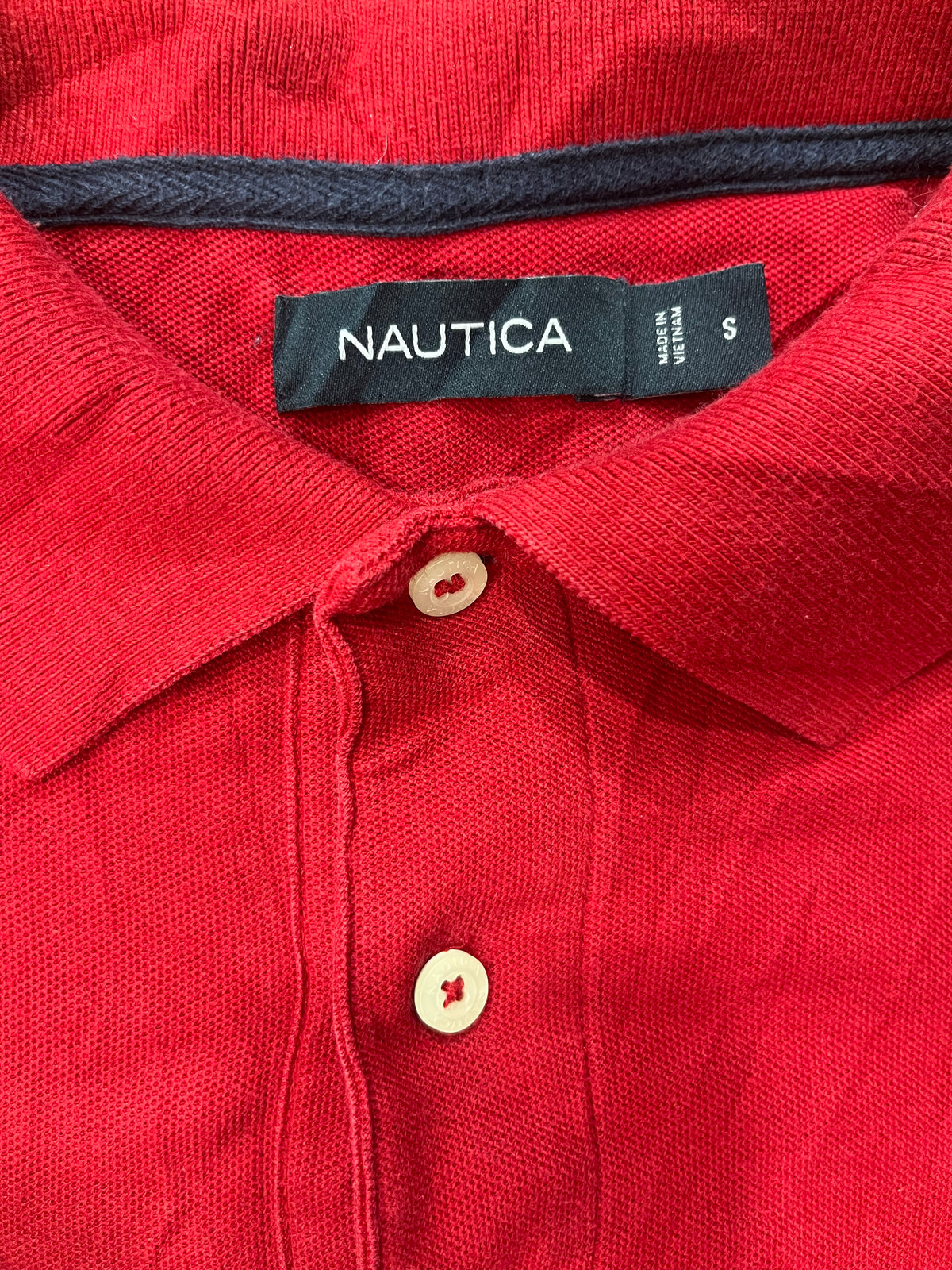 Close-up of a red knit polo shirt collar with a black Nautica neck label and cream buttons.