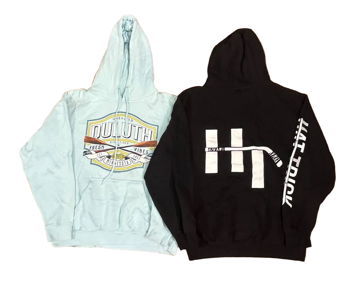 Two hoodies a light blue hoodie with a large multicolor chest graphic reading 'Duluth' and a black hoodie with a large white hockey-themed back graphic and vertical white text on the sleeve.