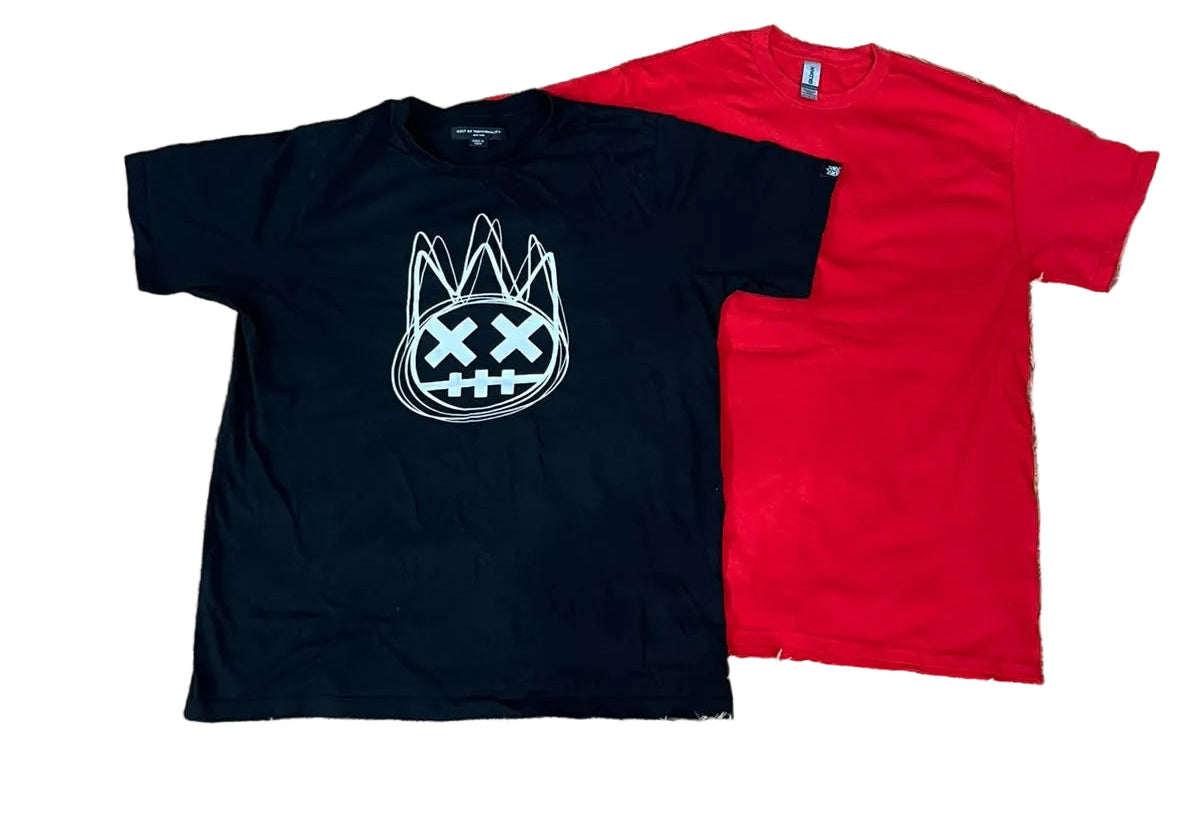 Two t-shirts one black with a white graphic of a cat head with an X for a mouth, and one bright red. Bare feet are visible at the bottom edge, and other folded clothes are scattered around the room.