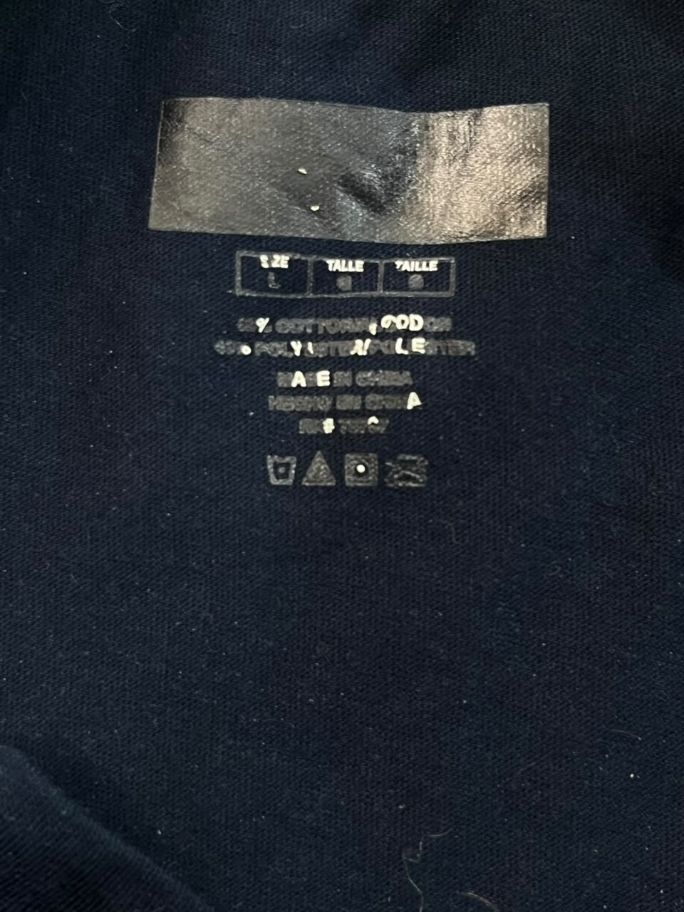 Close-up of the inside neck label of a dark navy blue garment, showing size information and care instructions.
