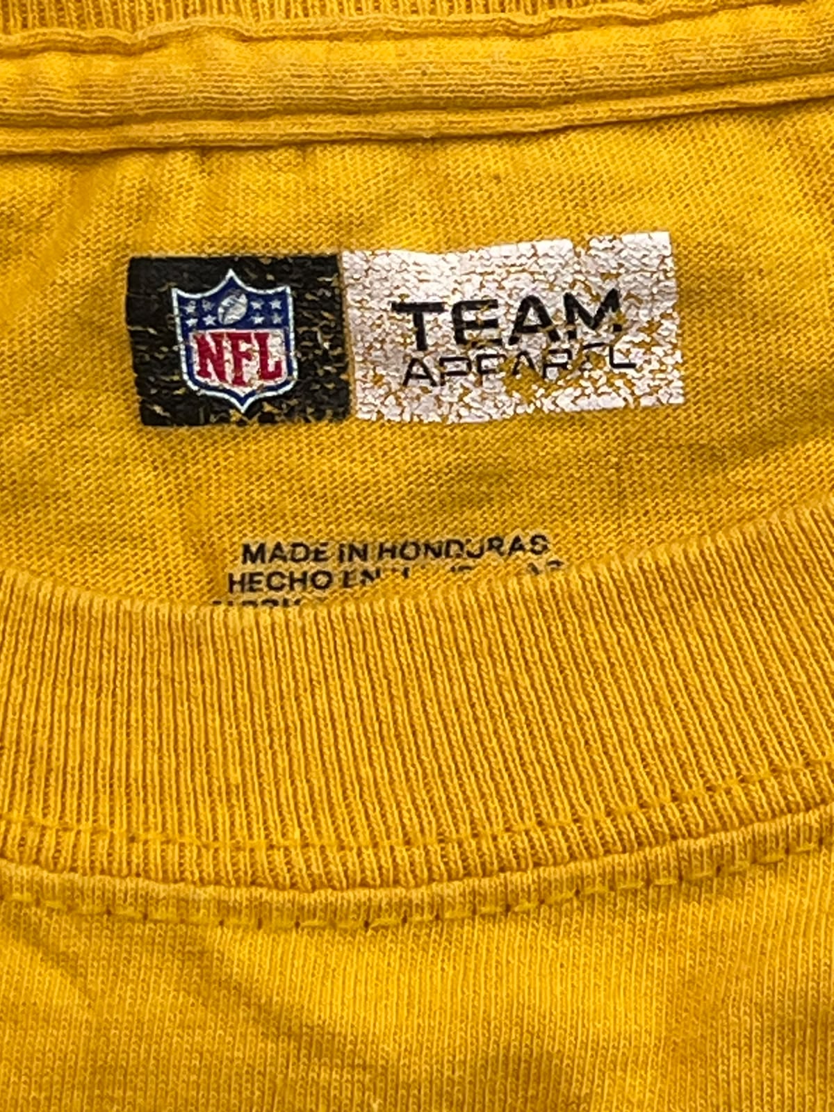 Close-up of a yellow ribbed knit garment showing an NFL and Team Apparel neck label.