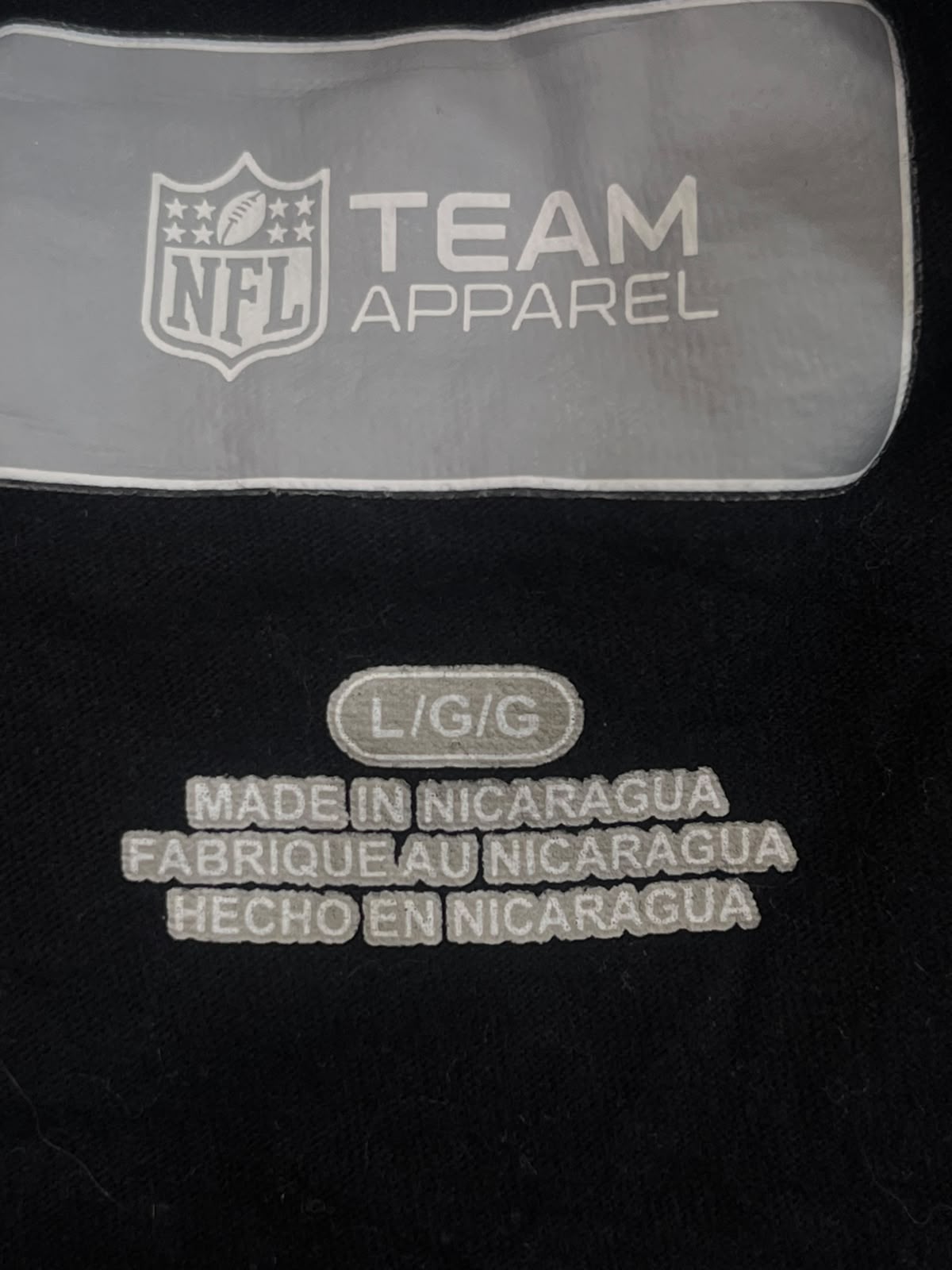 Close-up of a black garment showing an NFL Team Apparel label and embroidered text reading 'L/G/G' and 'MADE IN NICARAGUA FABRIQUE AU NICARAGUA HECHO EN NICARAGUA'.