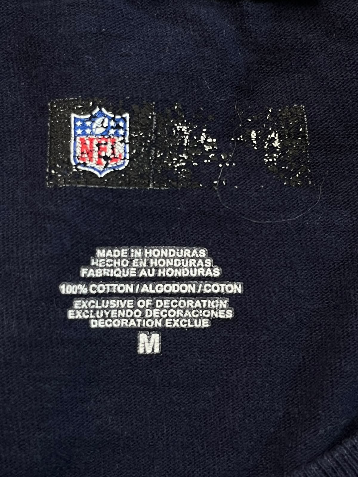 Close-up of a navy blue garment showing the NFL logo patch and size label text on the inside neck area.