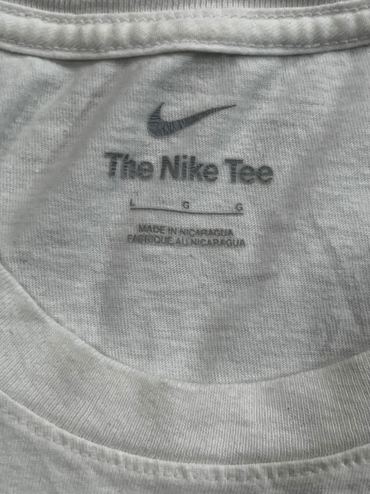 Close-up of the inside collar of a light gray Nike t-shirt, showing the printed Nike swoosh and 'The Nike Tee' text on the inner neck label.