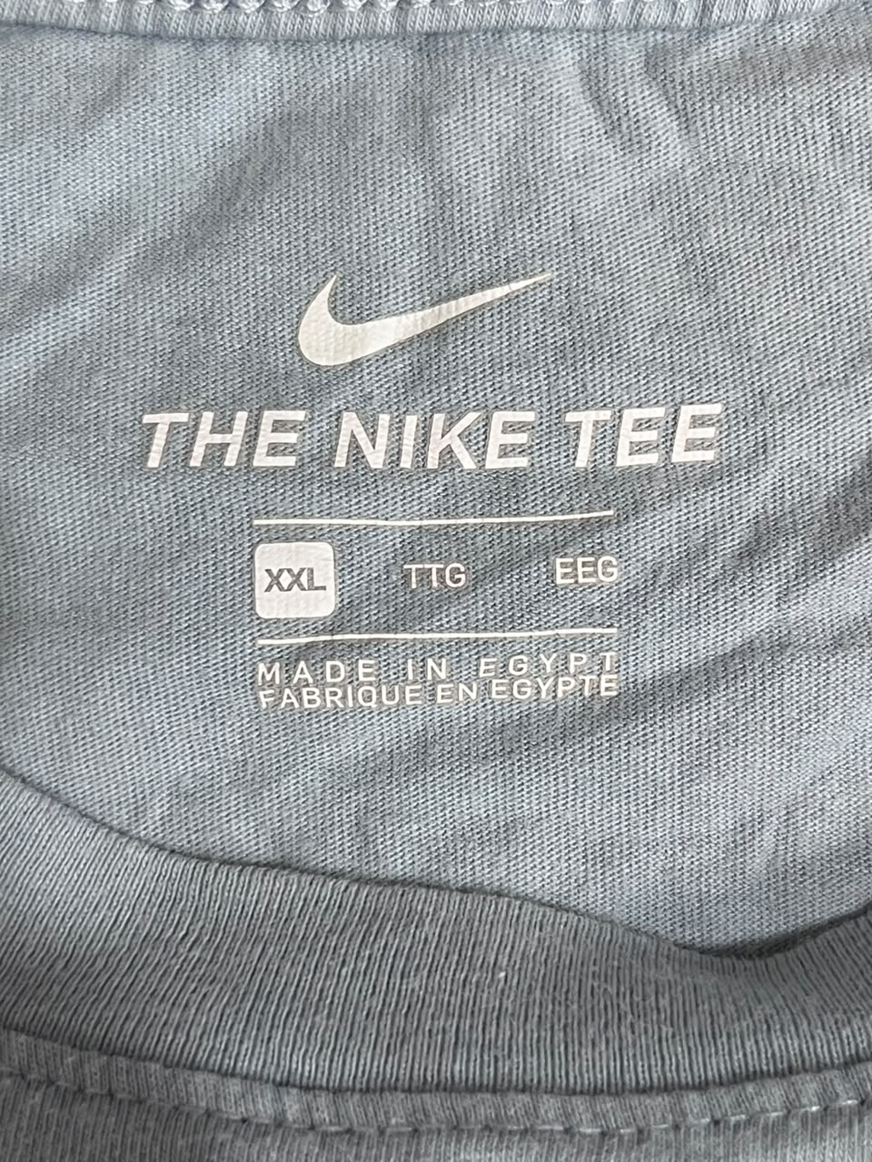 Close-up of a gray Nike t-shirt showing the inner neck label with a white Nike swoosh and 'THE NIKE TEE' text.