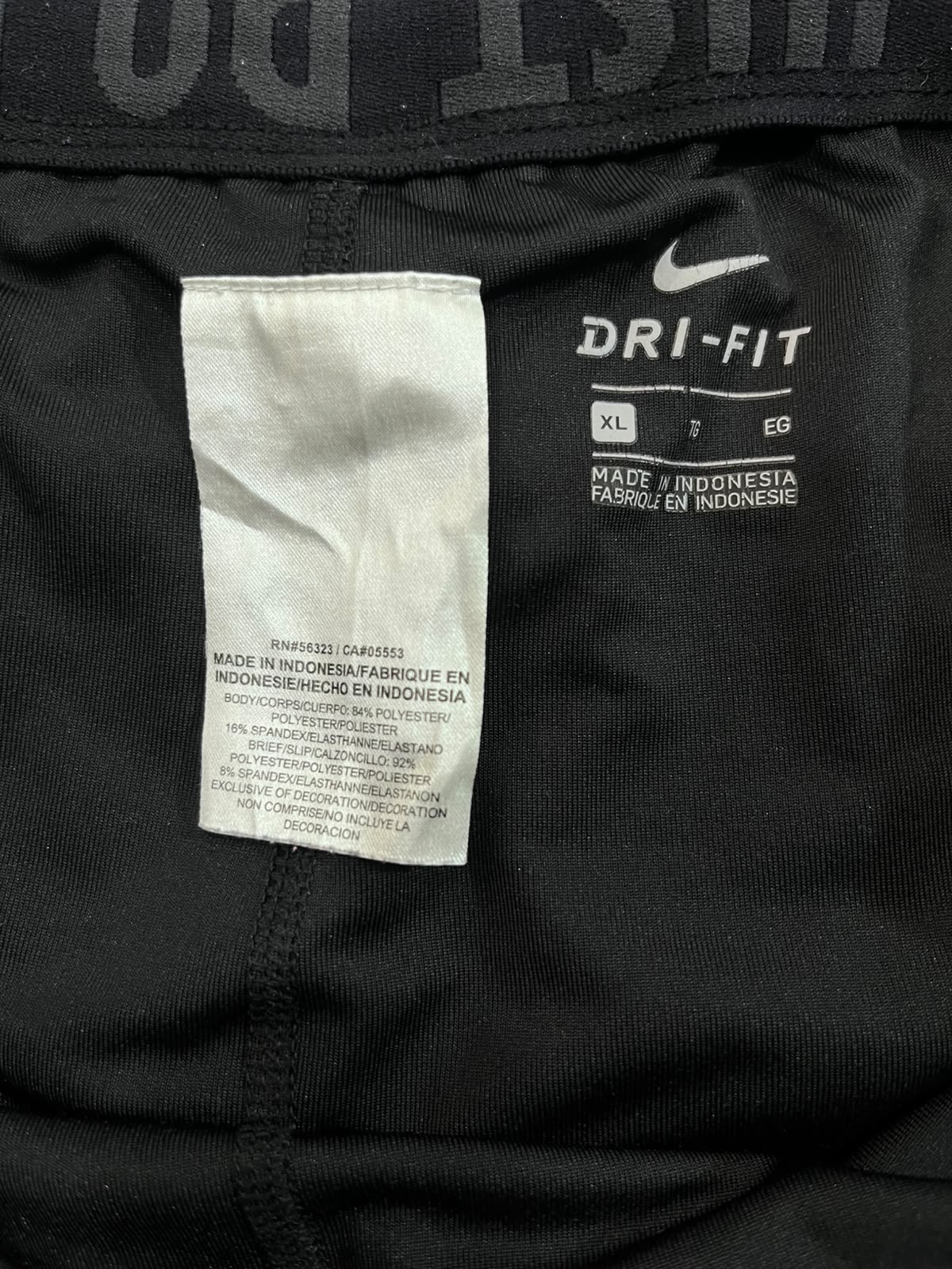 Close-up of the inside of a black Nike garment showing a white size tag and a white DRI-FIT logo patch.