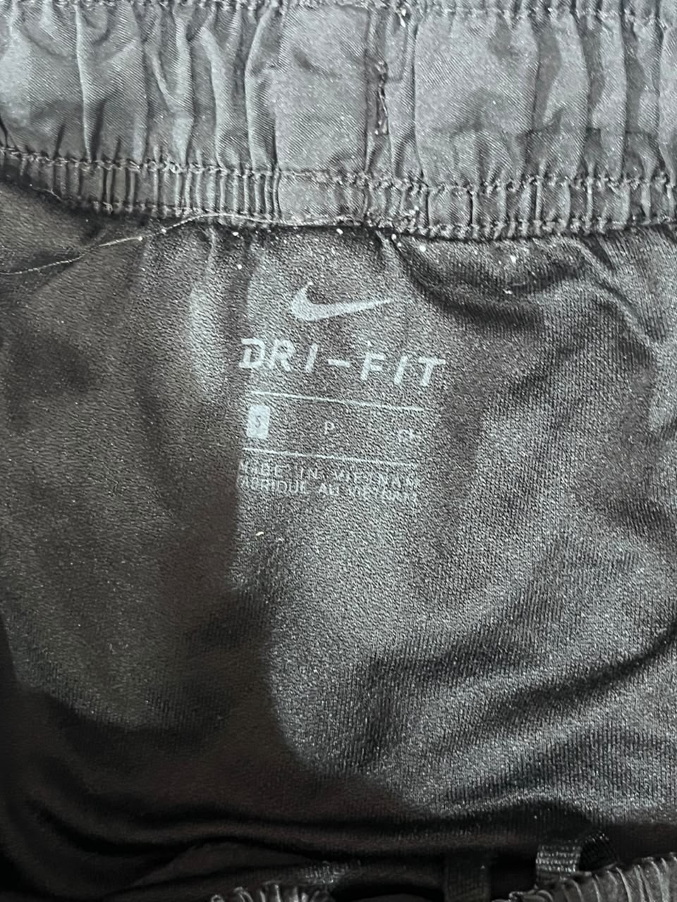 Close-up of the inside waistband of black Nike Dri-FIT athletic pants, showing the white Nike swoosh and Dri-FIT text printed on the fabric.