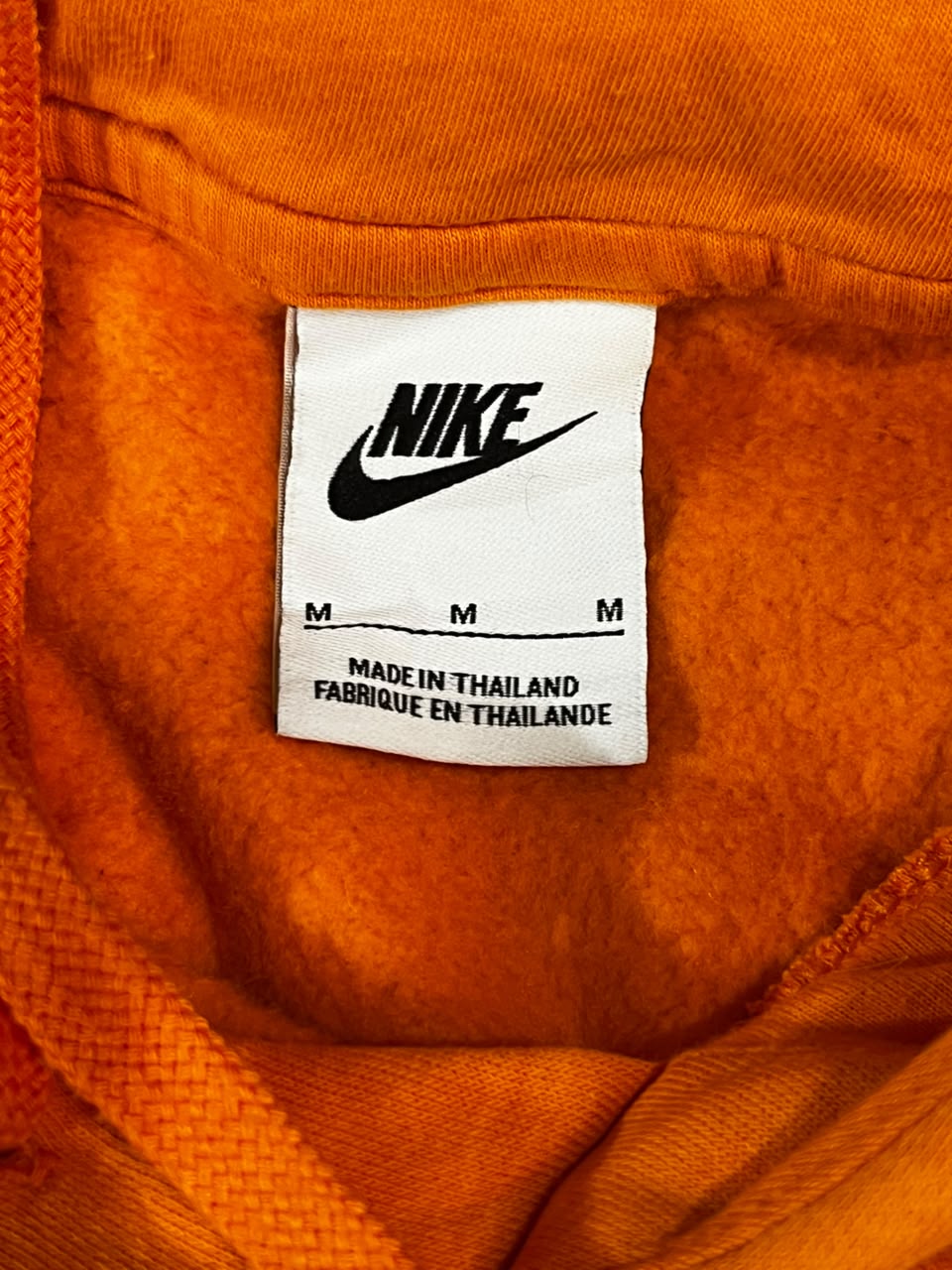 Close-up of a white Nike size tag with black logo and text reading 'MADE IN THAILAND' inside bright orange fabric.