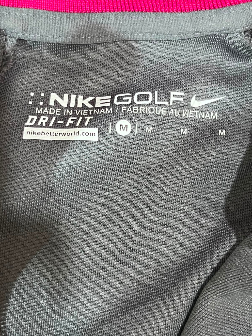 Close-up of a Nike Golf Dri-FIT garment interior label showing the Nike swoosh, 'Nike Golf', 'Made in Vietnam', and size M on dark gray fabric.