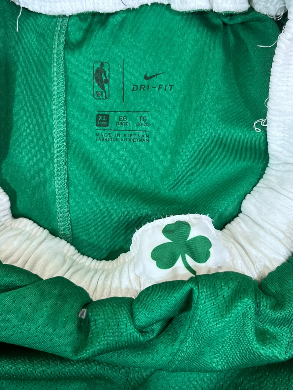 Close-up of a green Nike Dri-FIT garment with white fuzzy trim and a white patch featuring a green shamrock, showing the NBA logo, Nike swoosh, size information, and 'MADE IN VIETNAM' text.