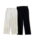 Two pairs of cropped pants one off-white/cream and one black. Bare feet are visible at the bottom edge, and other clothing is partially visible at the top.
