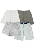 Four pairs of men's casual shorts in different colors (white, gray, light beige, and off-white) are laid flat on a speckled gray floor.