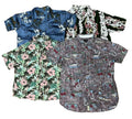 Four short-sleeve button-up shirts with tropical and nautical prints are arranged in a flat lay on a brown shag rug. The shirts feature various color palettes including blue, green, black, and gray, with floral and boat motifs.