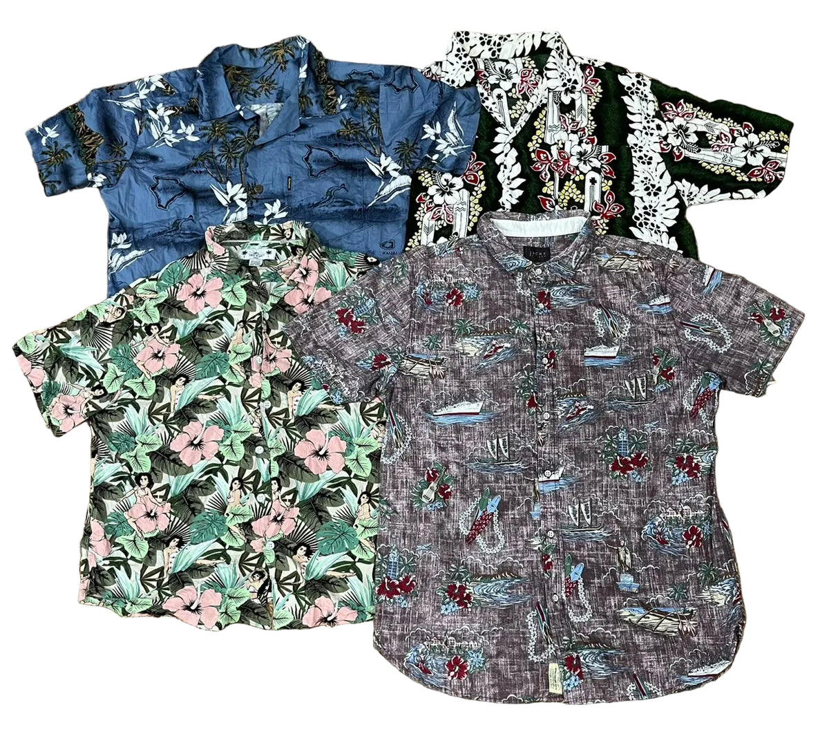 Four short-sleeve button-up shirts with tropical and nautical prints are arranged in a flat lay on a brown shag rug. The shirts feature various color palettes including blue, green, black, and gray, with floral and boat motifs.