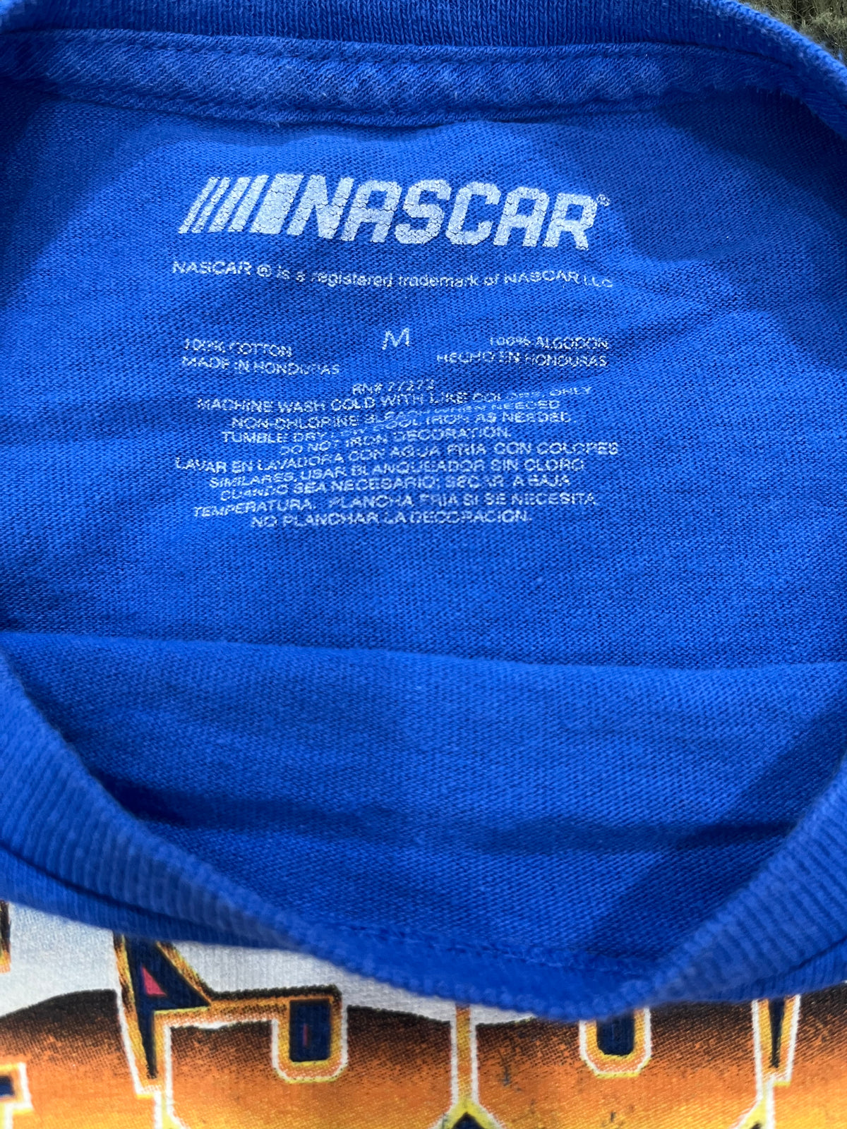 Close-up of the inside collar of a blue NASCAR t-shirt, showing the white printed NASCAR logo and care instructions on the inner neck label.