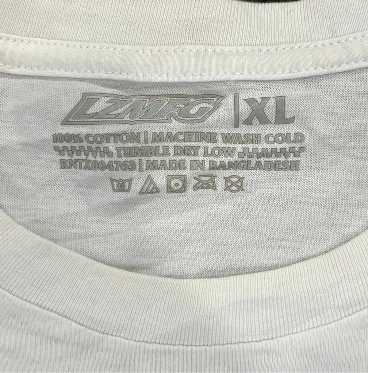 Close-up of the inside collar of a white cotton t-shirt showing the printed size XL and care instructions, placed against a dark green textured background.