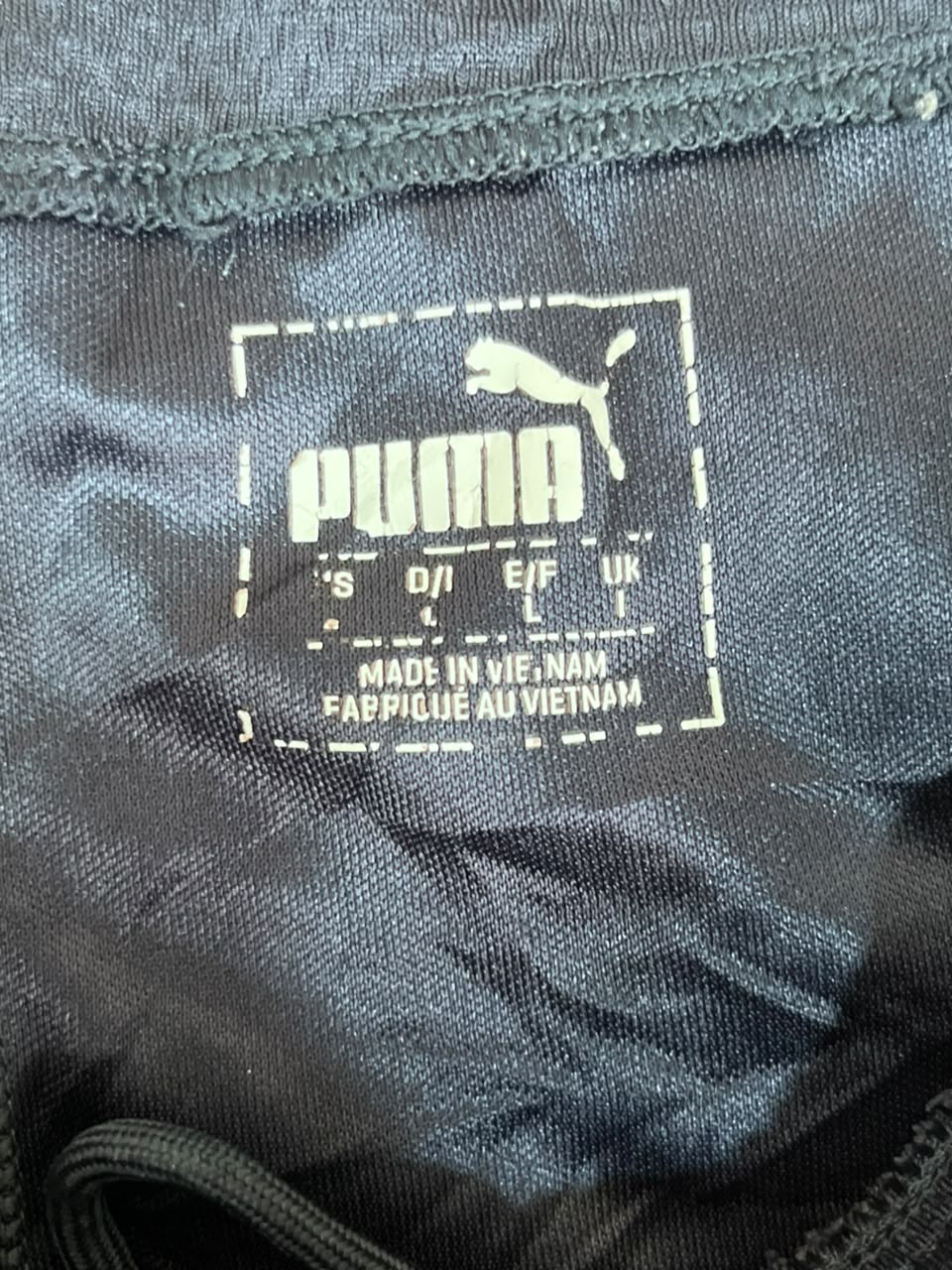 Close-up of a Puma garment interior label showing the Puma logo, size information, and 'Made in Vietnam' text on dark gray fabric.
