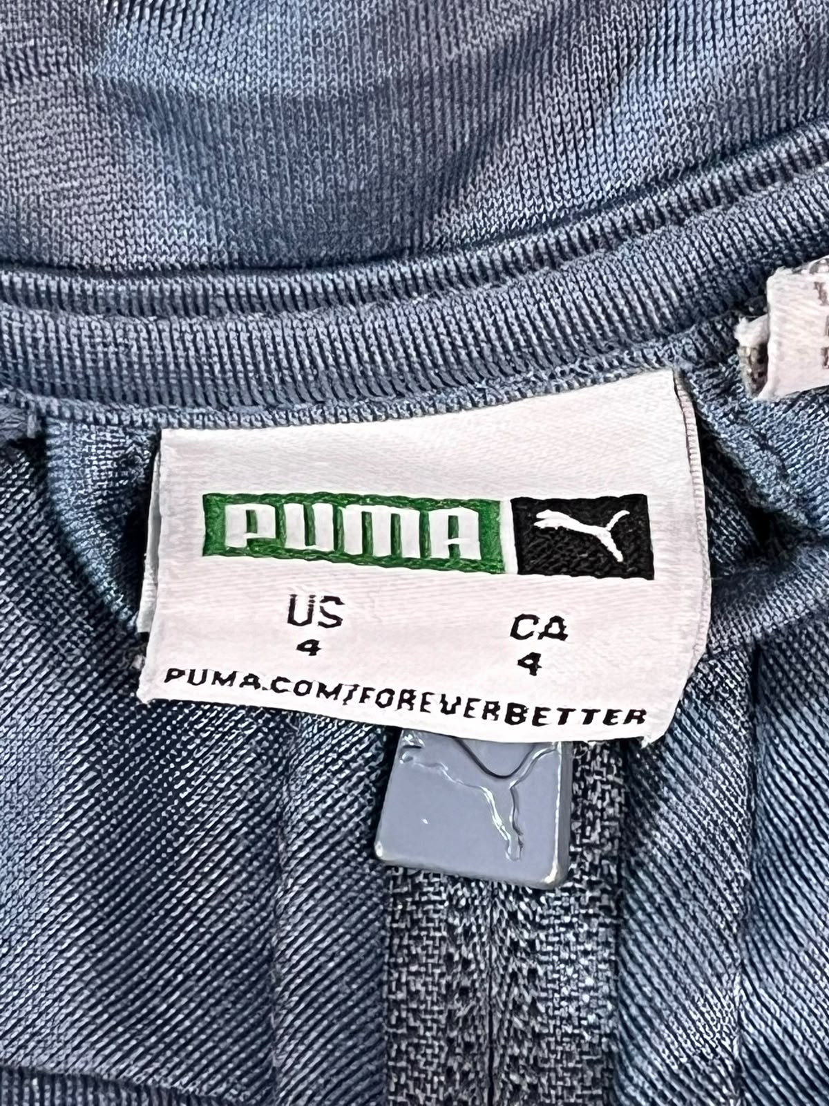 Close-up of a Puma garment label sewn inside the waistband of blue denim jeans, showing the Puma brand logo and size information.