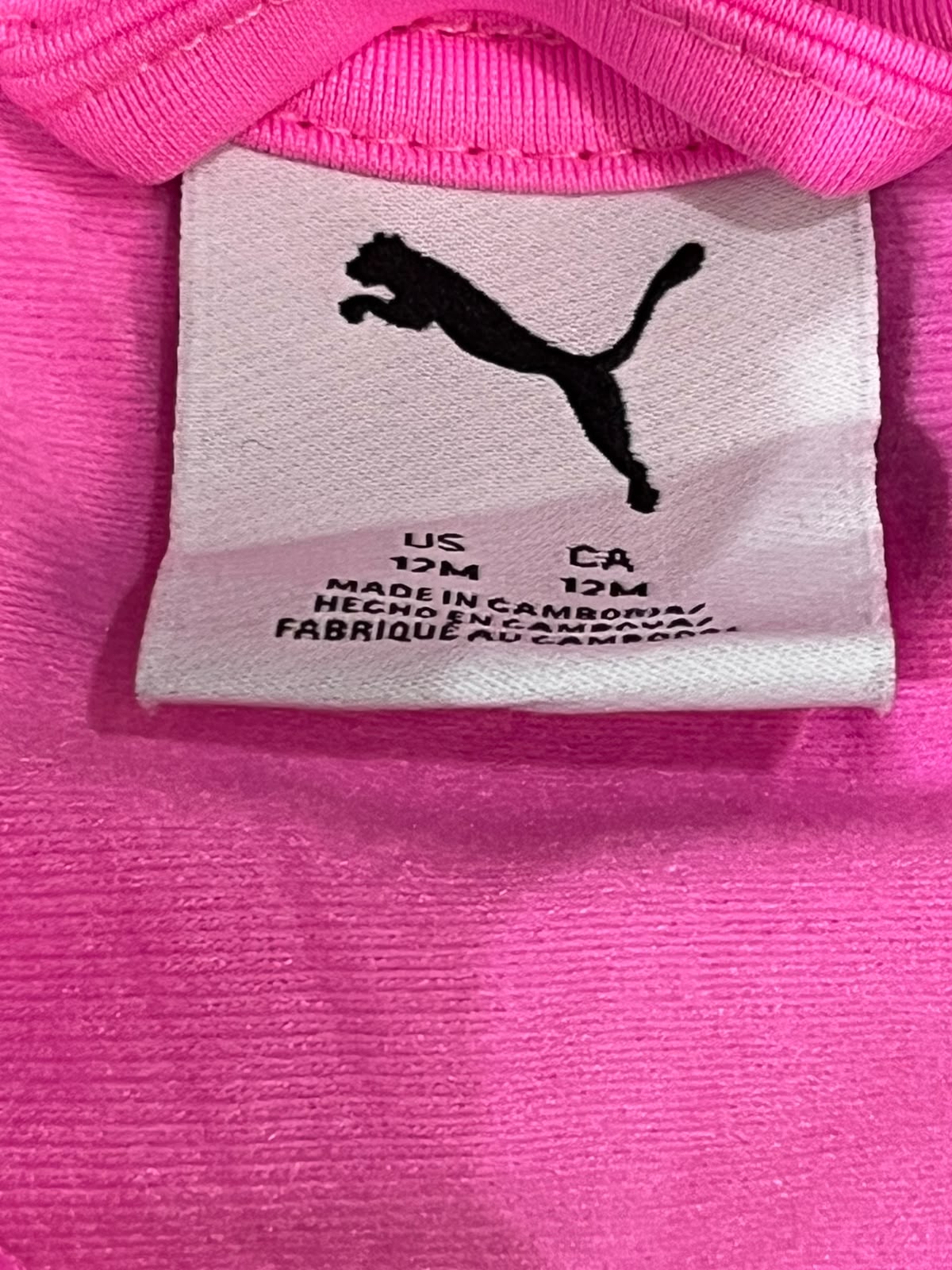 Close-up of a bright pink Puma garment showing the interior neck label with the black Puma leaping cat logo and size text.