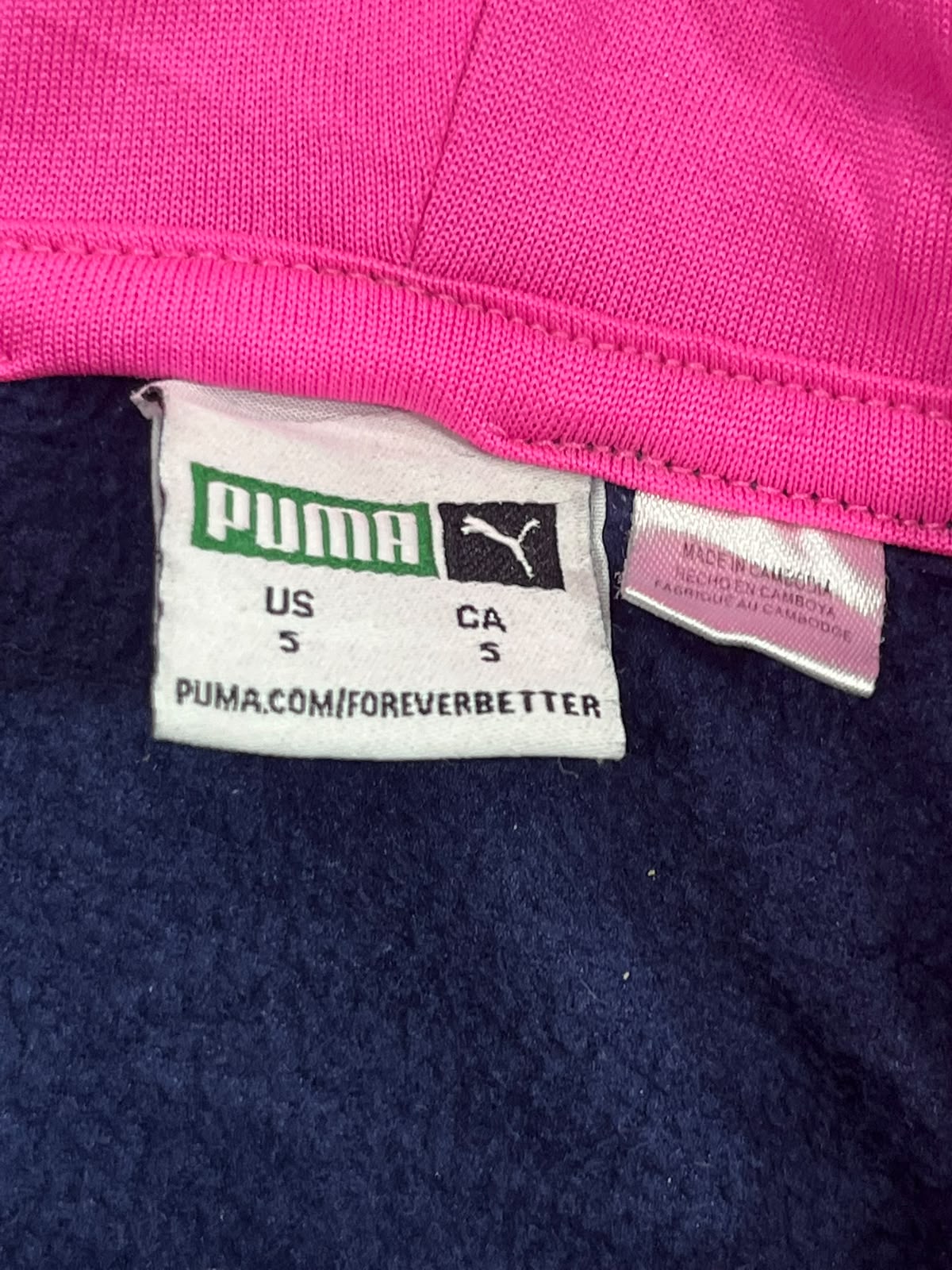 Close-up of a Puma garment label on a pink and navy fleece or jersey top, showing the Puma logo and Forever Better slogan.