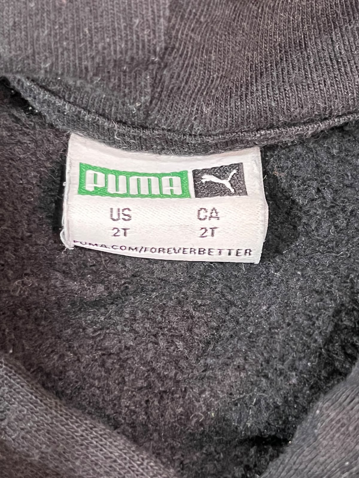 Close-up of a Puma garment label sewn inside the collar of a dark gray knit top, showing the Puma cat logo and size information.