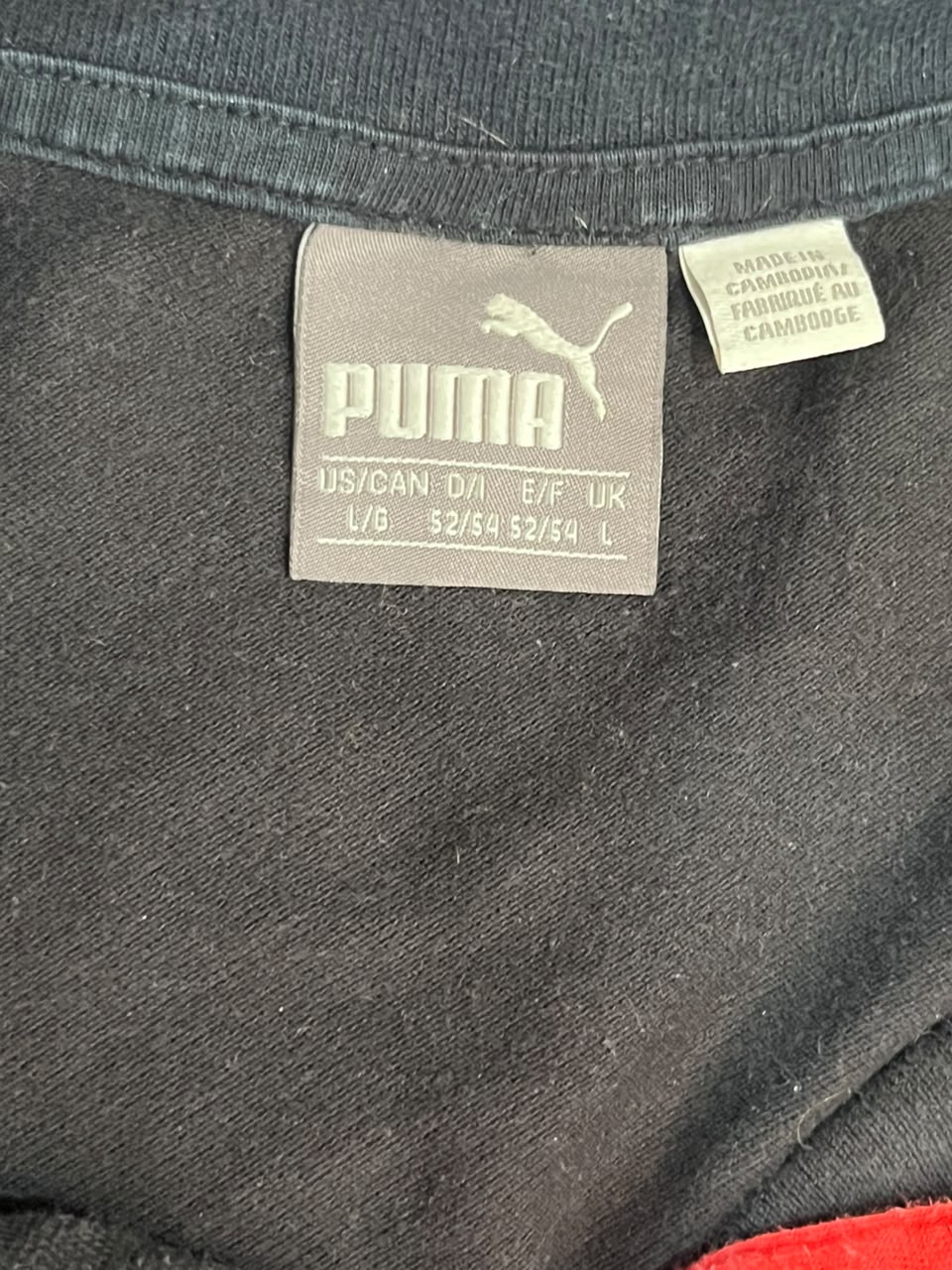 Close-up of a Puma garment label sewn onto dark charcoal gray fabric, with a small white care tag beside it.